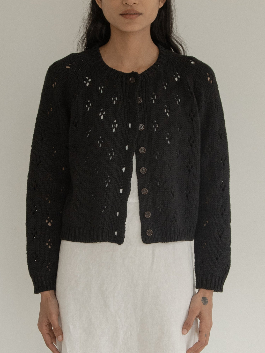 Model wearing the Mabel Cardigan in Noir by Gillian Stevens, front view showing eyelet detail