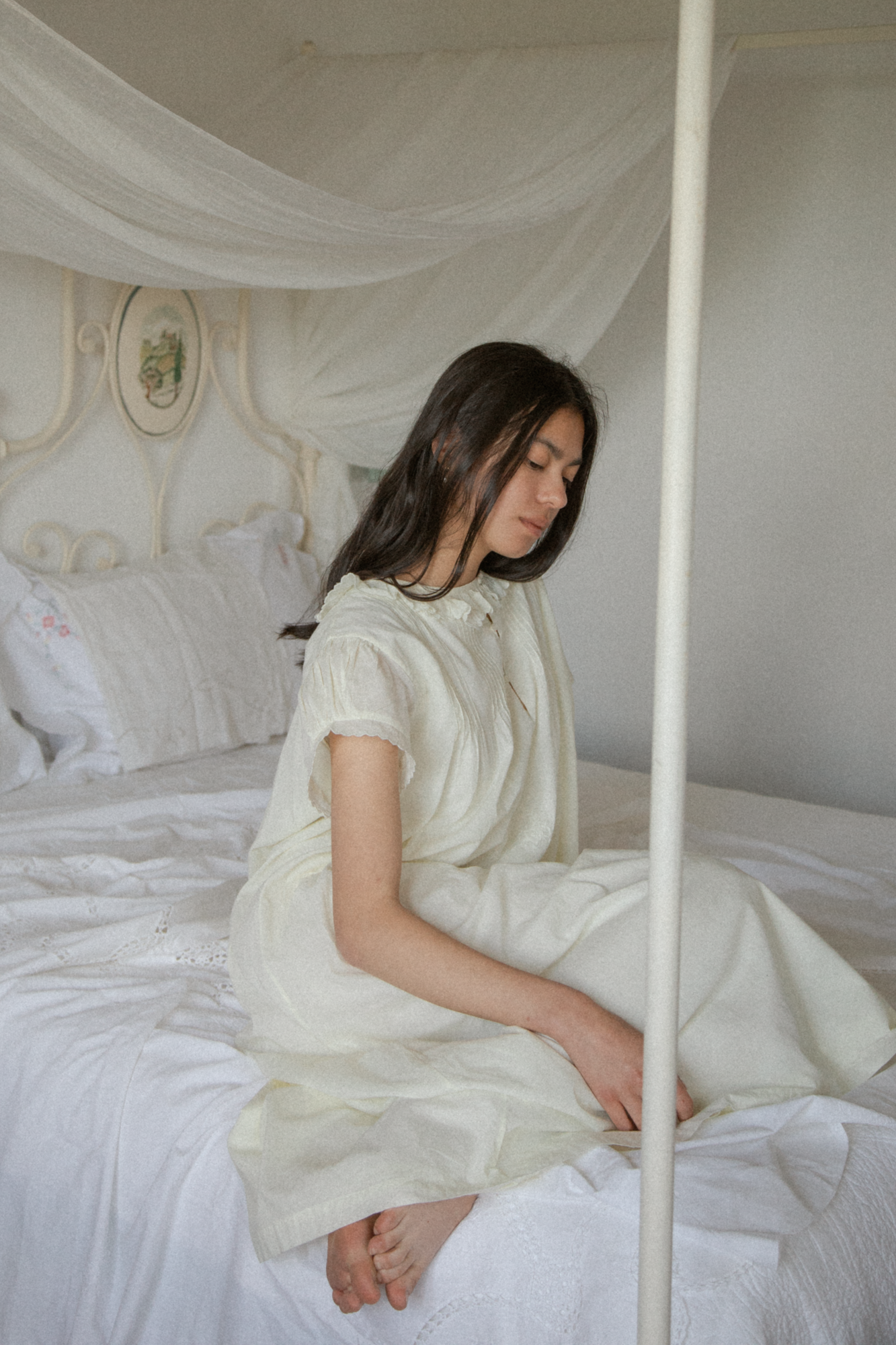 Model seated on a canopy bed wearing the Clover Dress in Butter by Gillian Stevens, side view