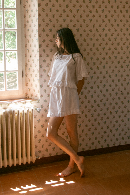 Model wearing the Arlette Short in Salt by Gillian Stevens, side view by a sunlit window