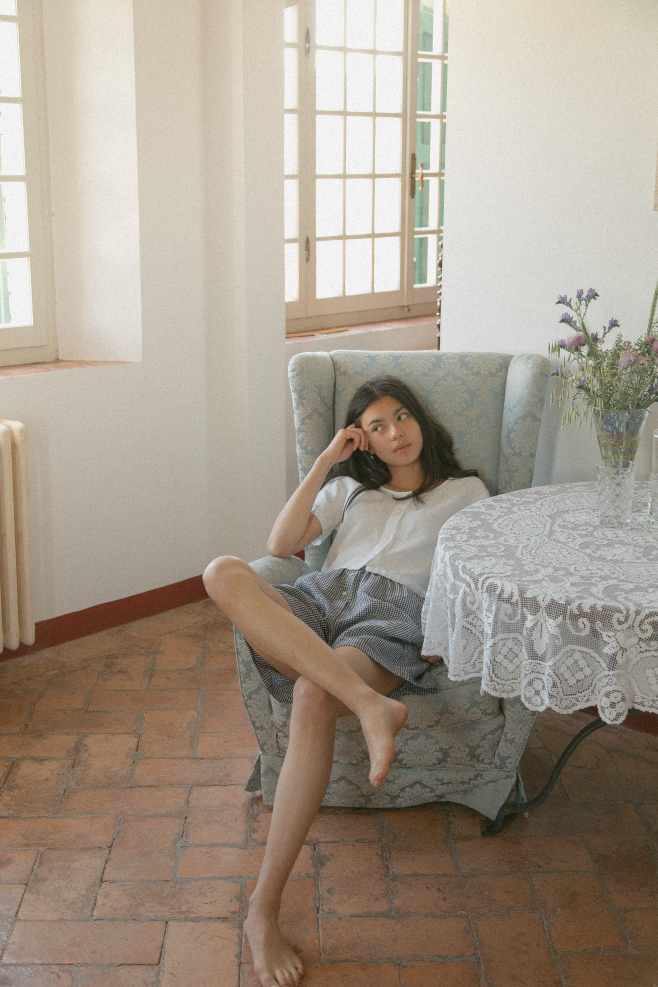 Model wearing the Wren Top in Salt by Gillian Stevens, seated in an armchair in a sunlit room