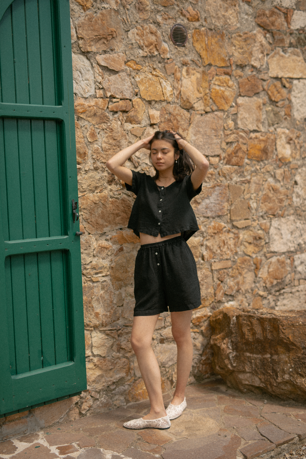 Model wearing the Wren Top in Noir by Gillian Stevens, front view against a rustic stone wall