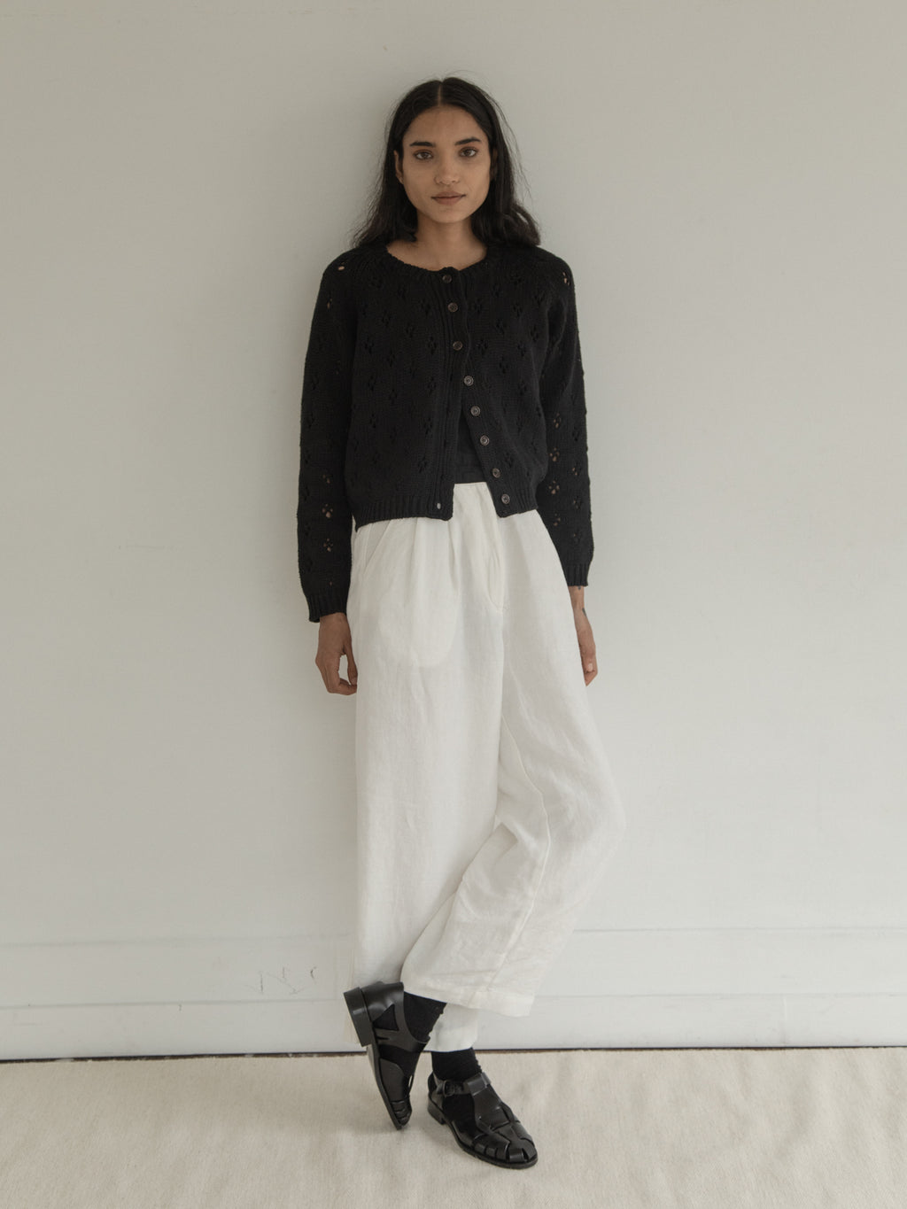 Model wearing the Mabel Cardigan in Noir by Gillian Stevens, full-length front view with white trousers, view 2