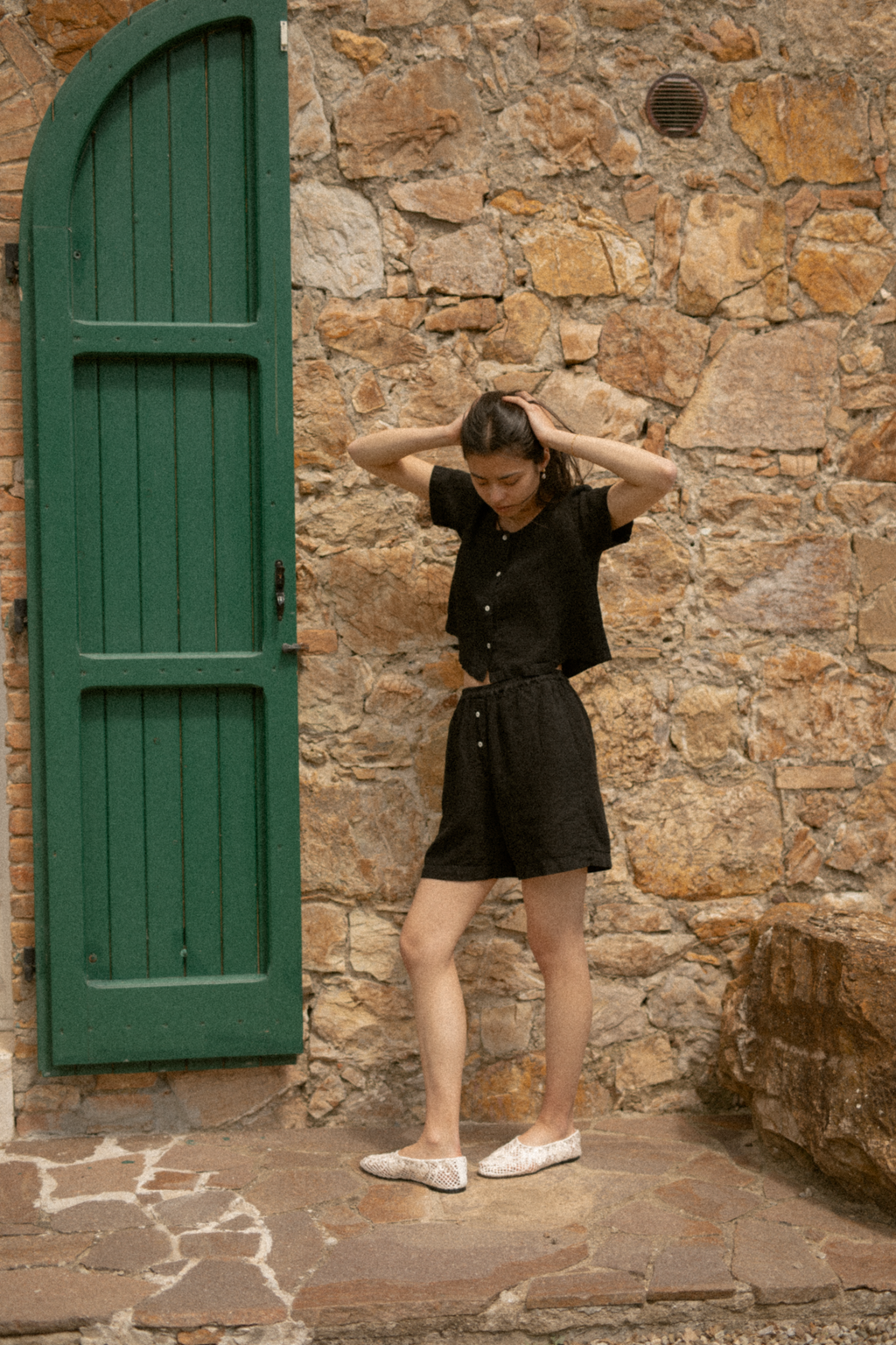 Model wearing the Wren Top in Noir by Gillian Stevens, styled with matching shorts beside a stone wall