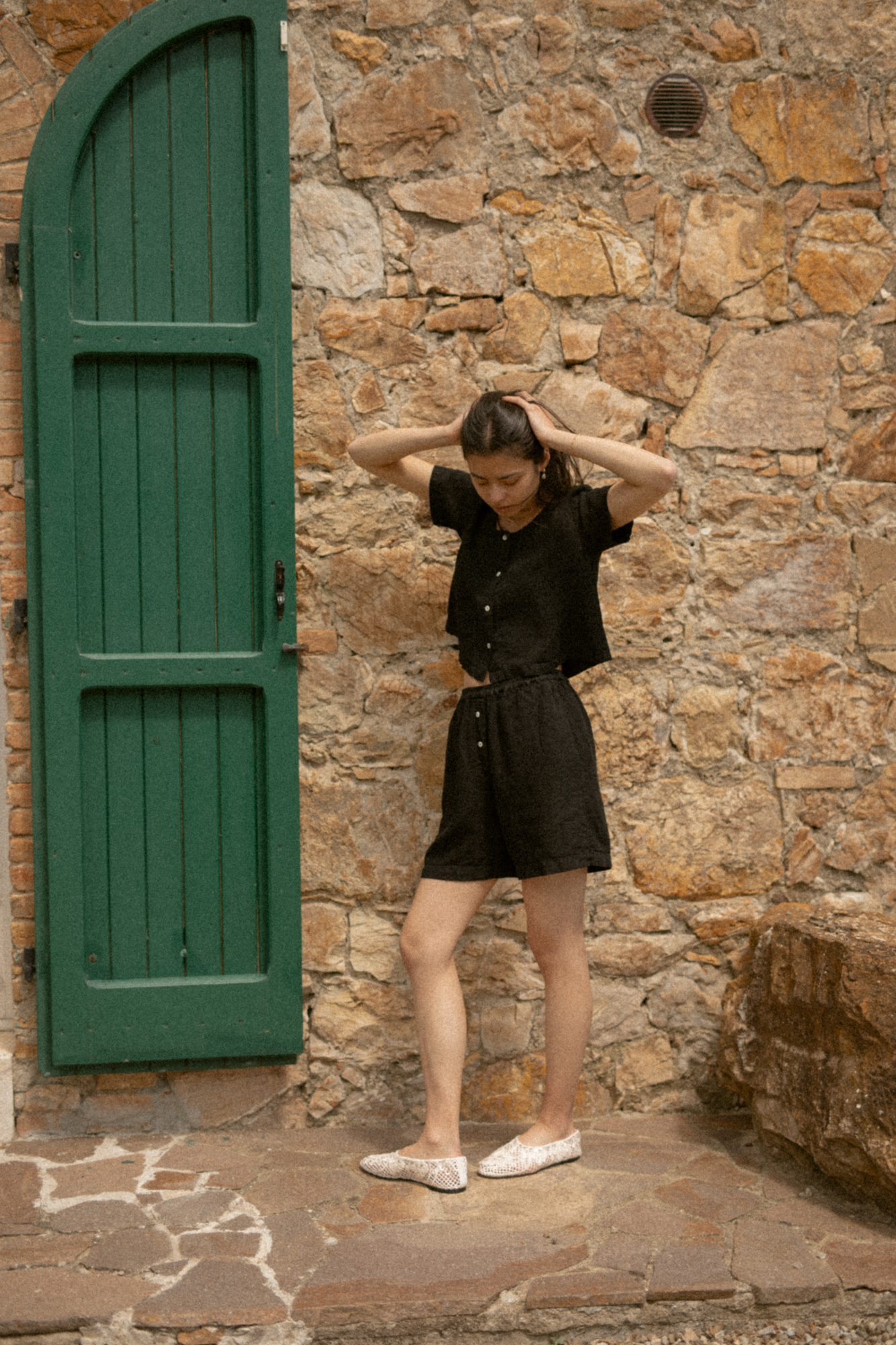 Model wearing the Wren Top in Noir by Gillian Stevens, styled with matching shorts beside a stone wall