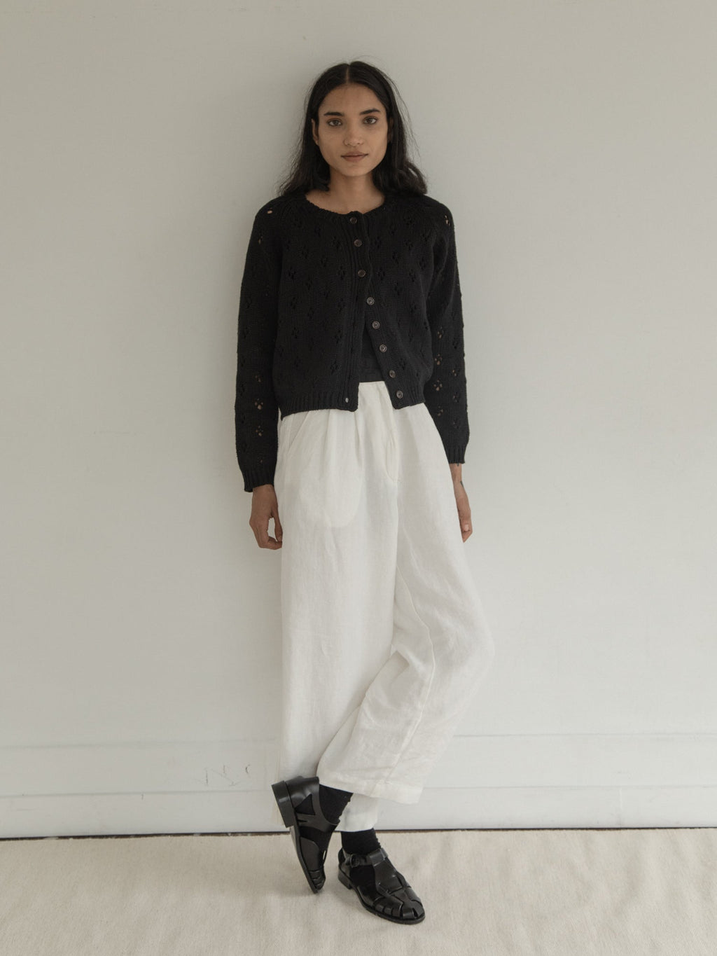Model wearing the Mabel Cardigan in Noir by Gillian Stevens, full-length front view with white trousers