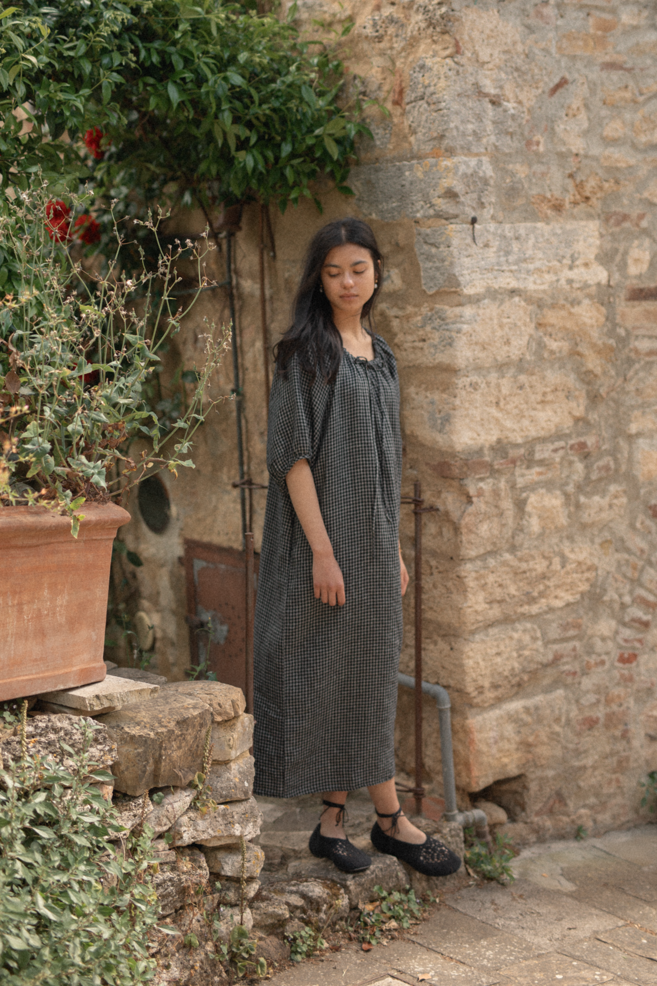 Model wearing the Jones Dress in Black Check by Gillian Stevens, full-length side view against a stone wall