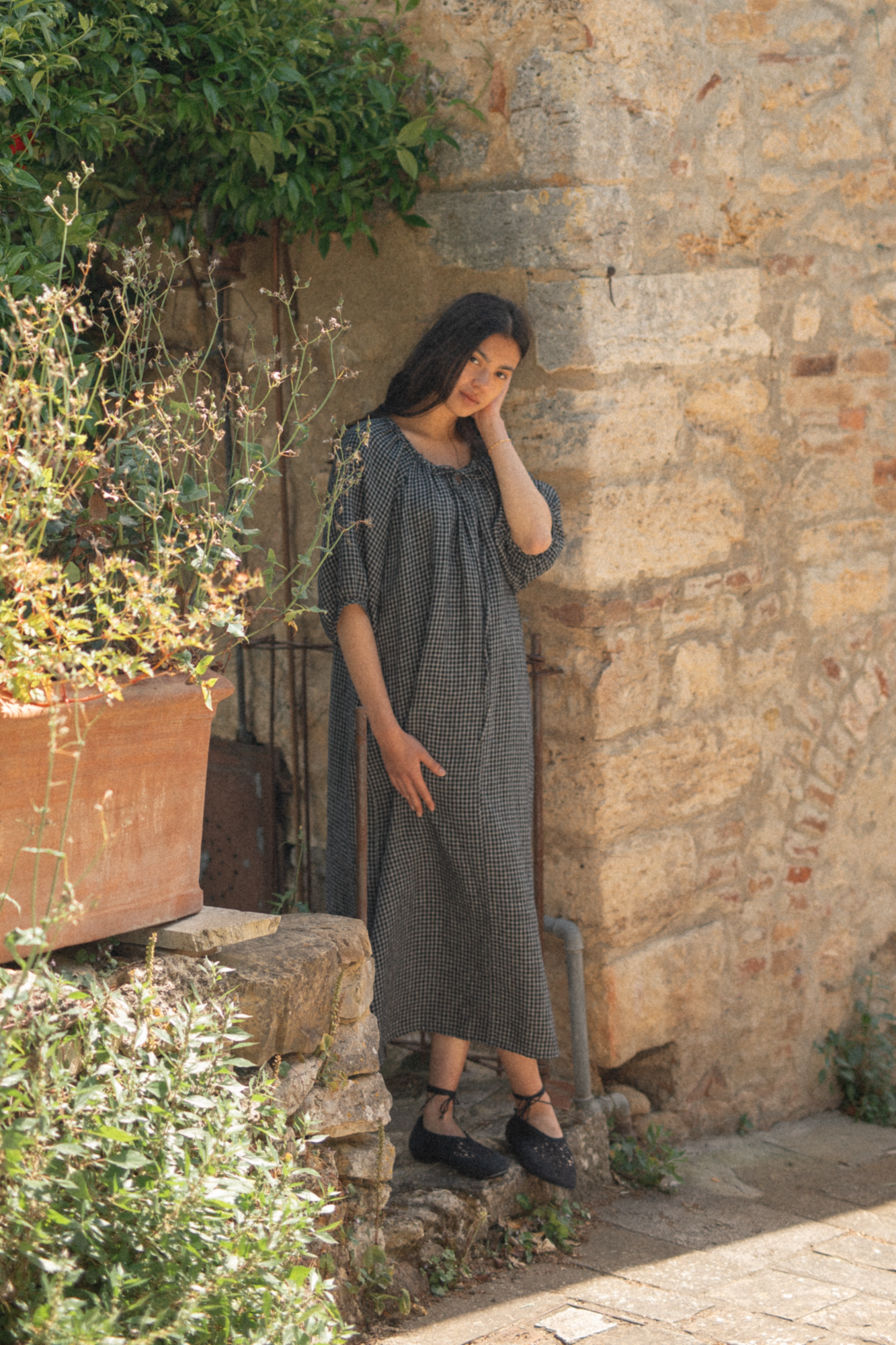 Model wearing the Jones Dress in Black Check by Gillian Stevens, front view against a rustic stone wall