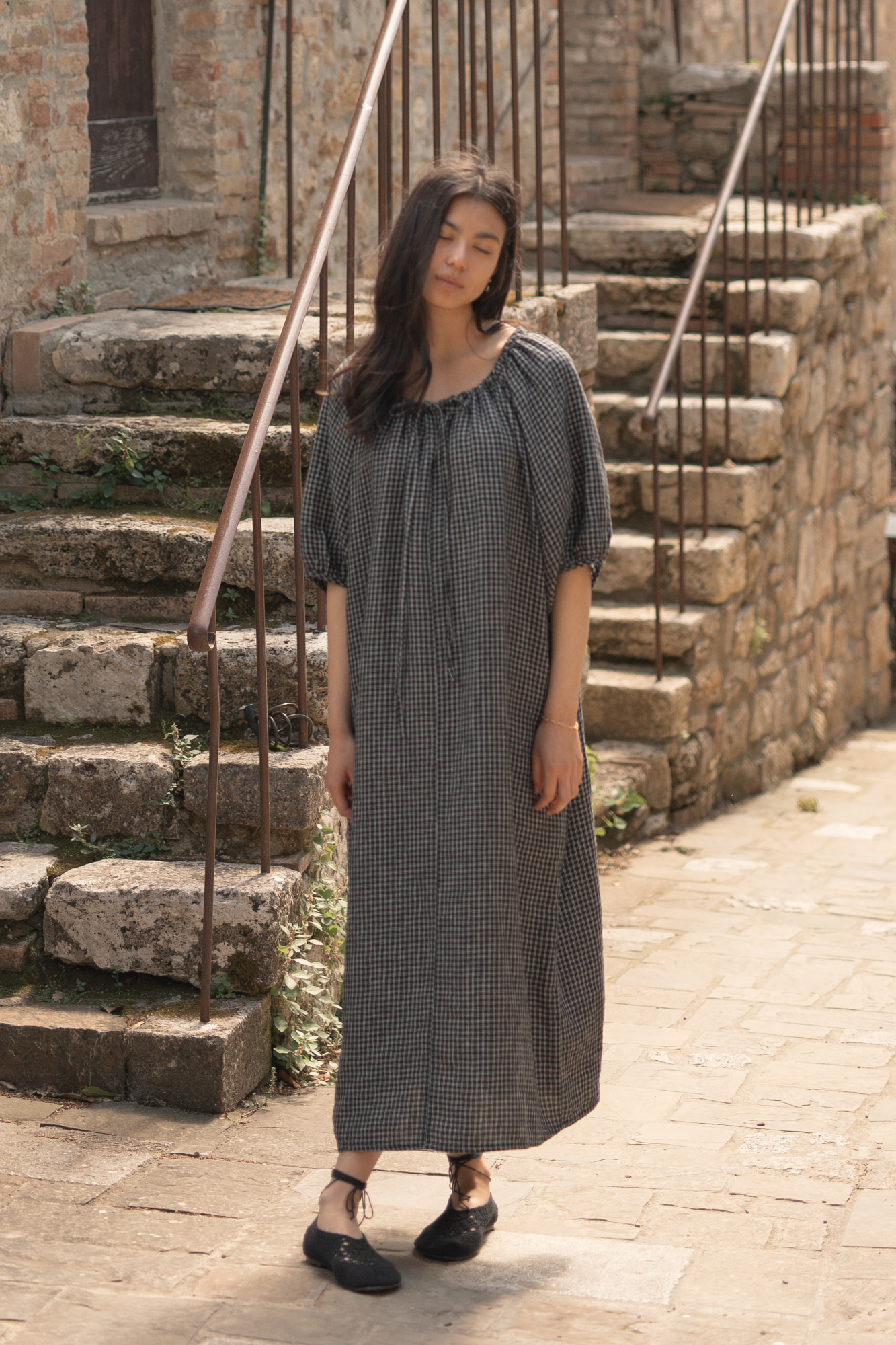 Model wearing the Jones Dress in Black Check by Gillian Stevens, front view on a cobblestone street