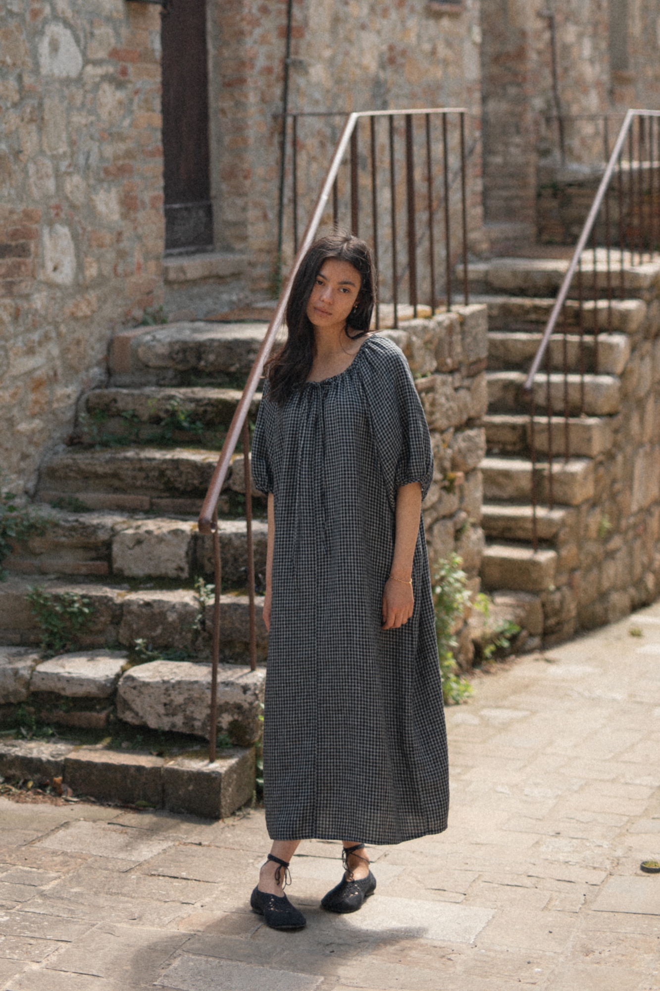 Model wearing the Jones Dress in Black Check by Gillian Stevens, front view on a cobblestone street