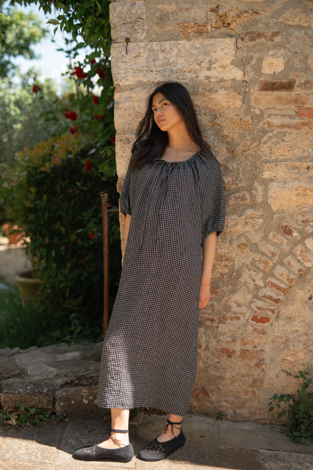 Model wearing the Jones Dress in Black Check by Gillian Stevens, front view against a rustic stone wall