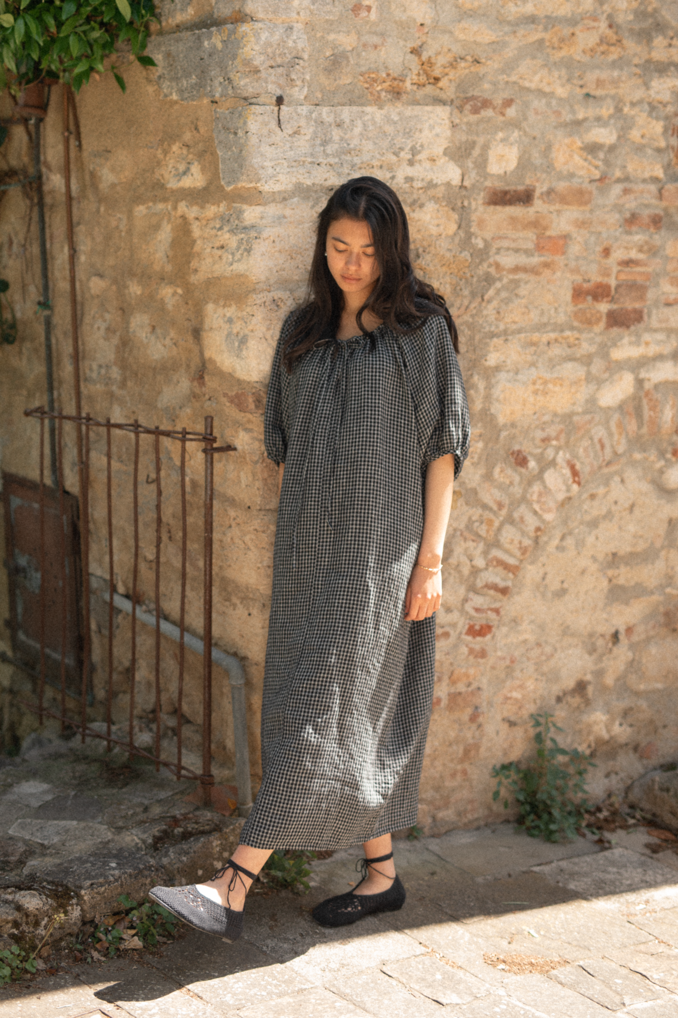 Model wearing the Jones Dress in Black Check by Gillian Stevens, full-length front view against a stone wall