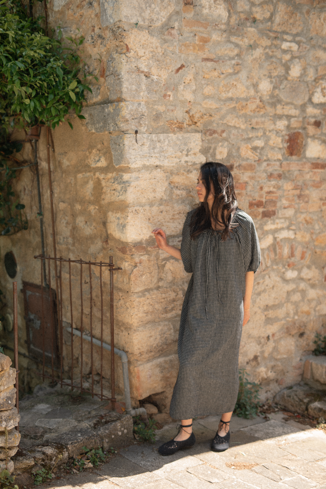 Model wearing the Jones Dress in Black Check by Gillian Stevens, back view against a rustic stone wall
