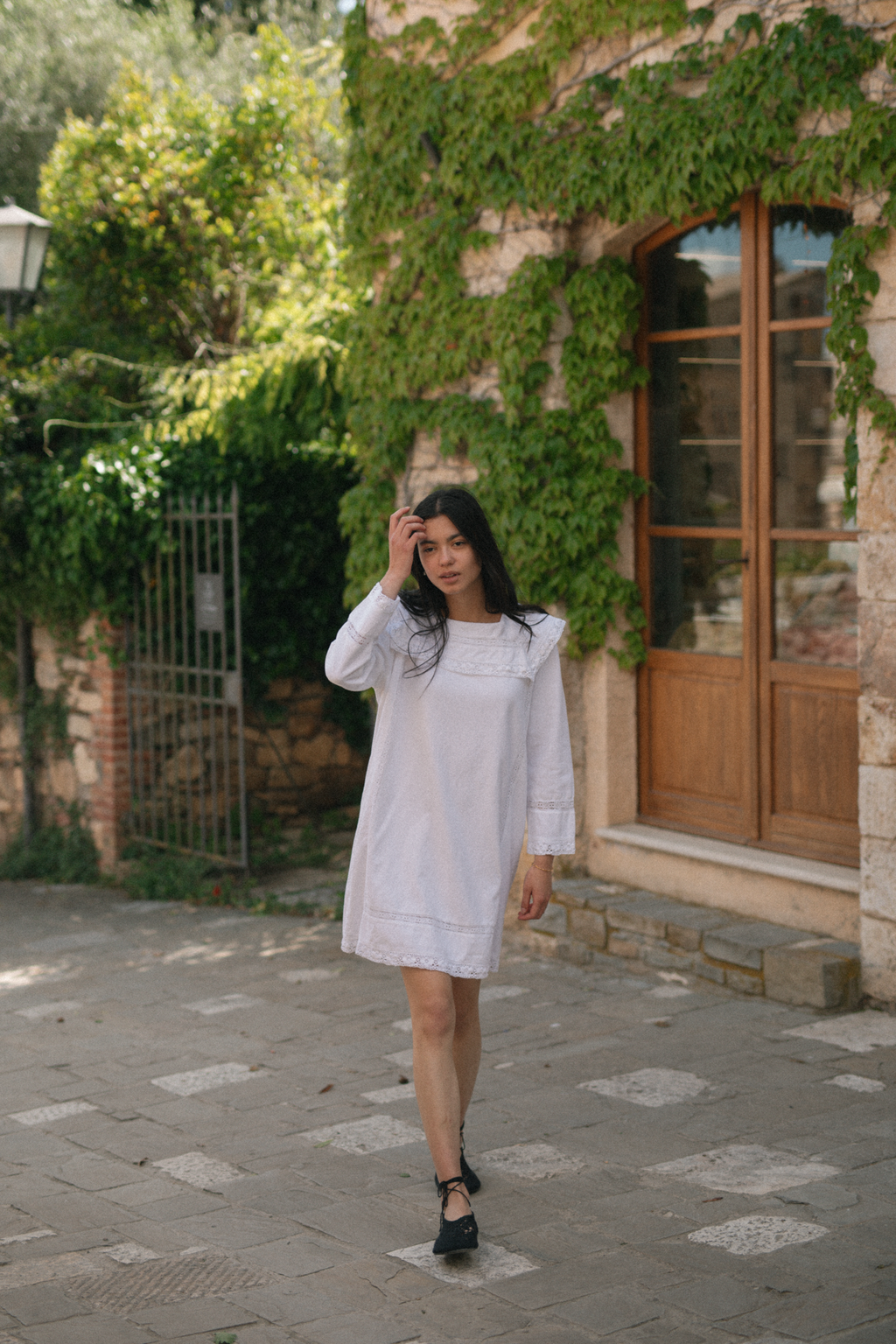 Model wearing the Laine Dress in Salt by Gillian Stevens, full-length front view on a cobblestone courtyard