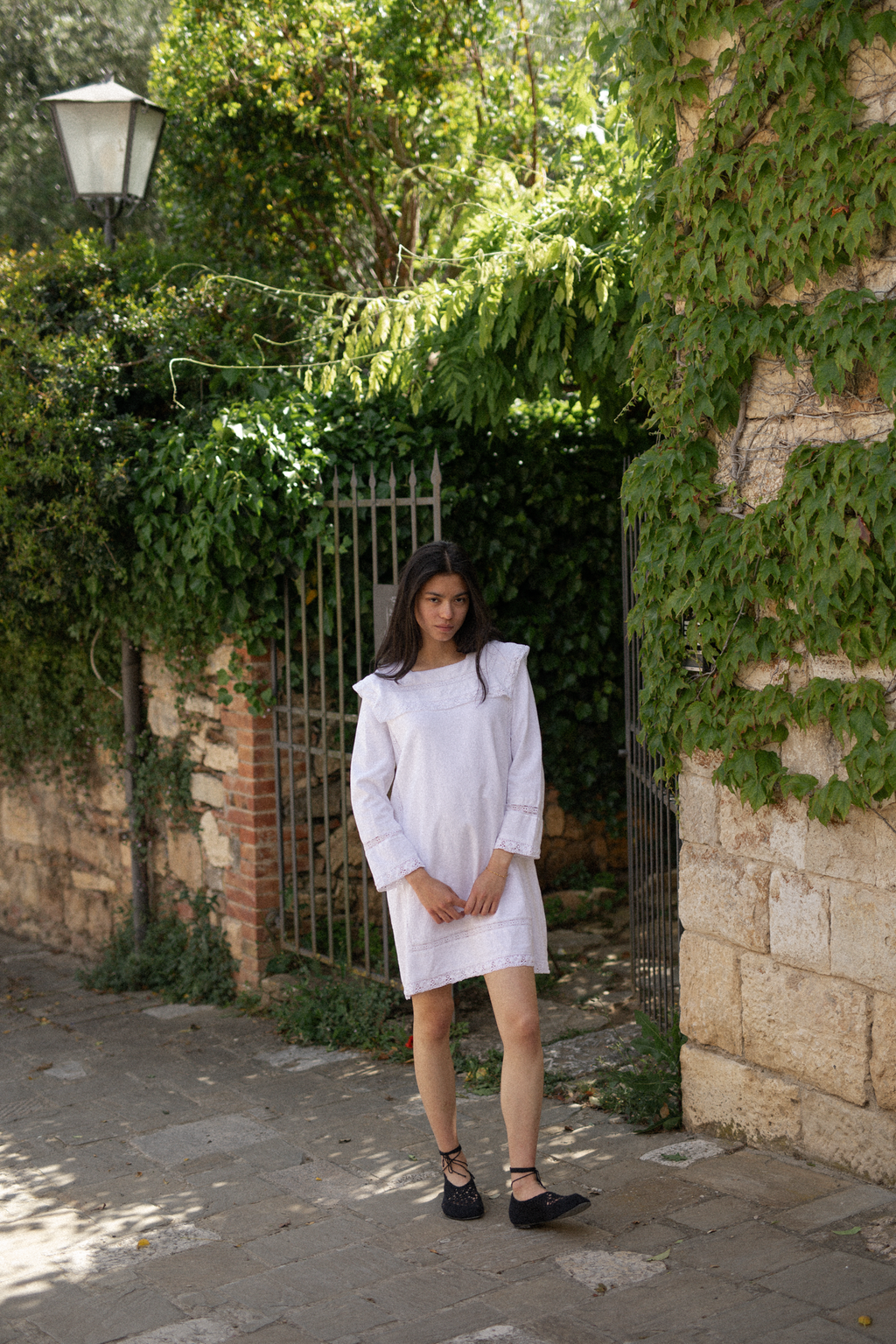 Model wearing the Laine Dress in Salt by Gillian Stevens, full-length front view beside an ivy-covered stone gate