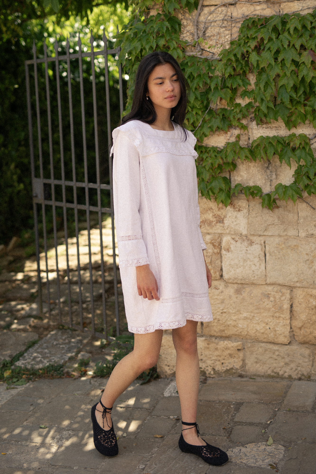 Model wearing the Laine Dress in Salt by Gillian Stevens, front view outdoors beside a stone wall