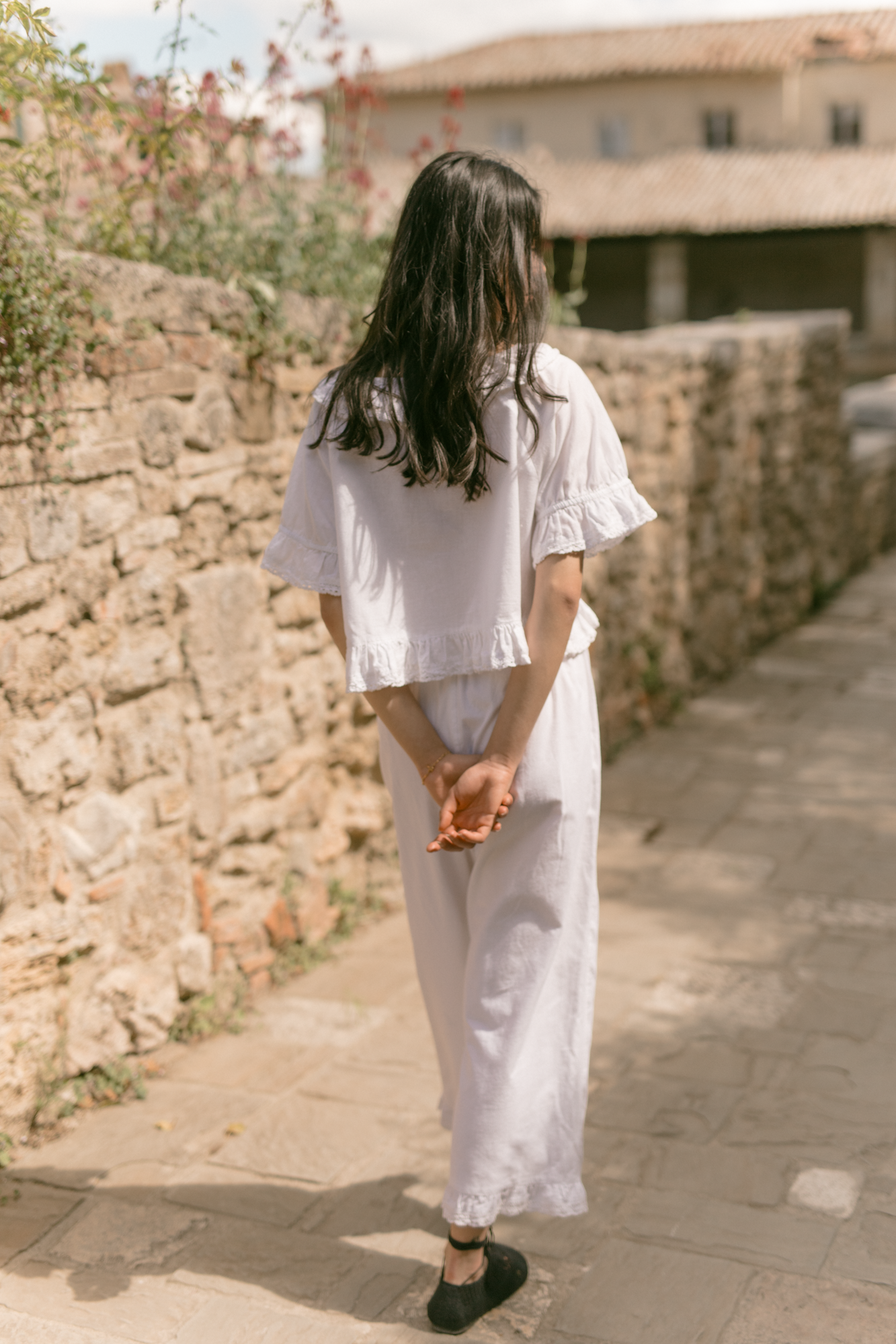 Model wearing the Arlette Pant in Salt by Gillian Stevens, back view on a sunlit cobblestone path