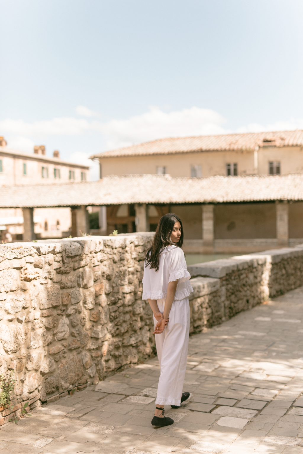 Model wearing the Arlette Pant in Salt by Gillian Stevens, three-quarter view at a Tuscan stone courtyard