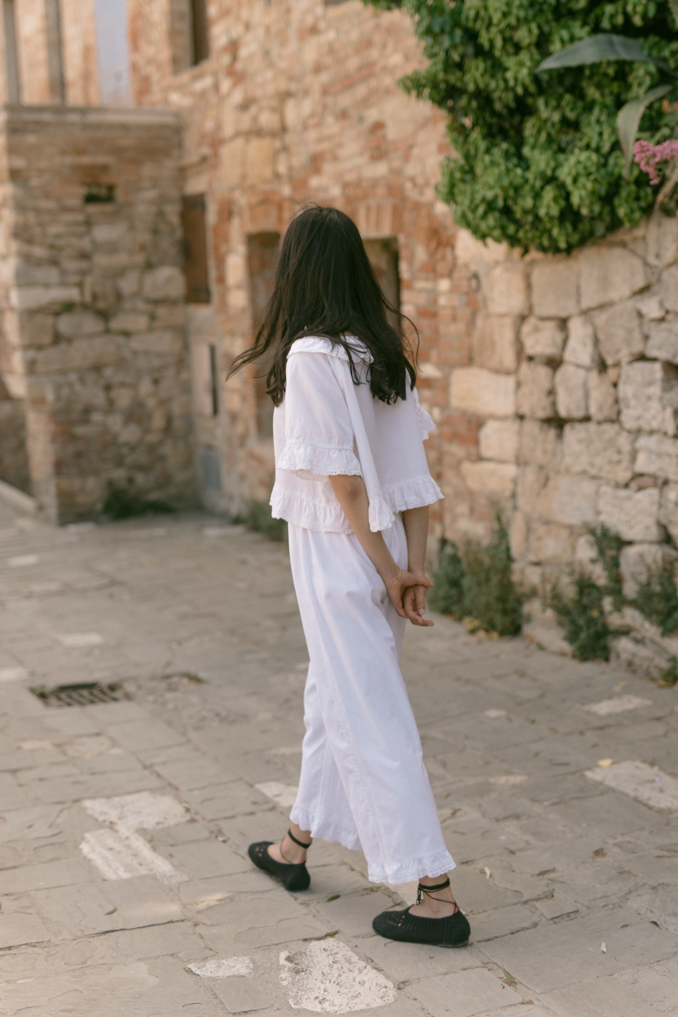 Model wearing the Arlette Pant in Salt by Gillian Stevens, back view on a cobblestone street