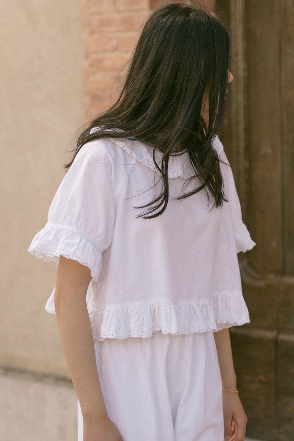 Model wearing the Arlette Top in Salt by Gillian Stevens, back view showing lace-trim ruffle hem and sleeves