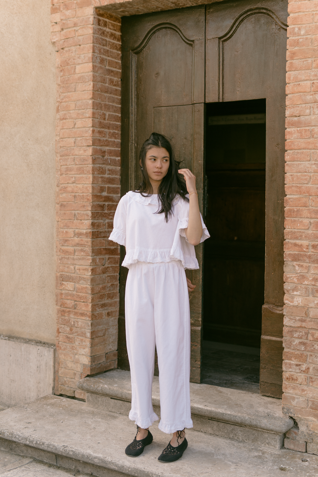 Model wearing the Arlette Pant in Salt by Gillian Stevens, full-length front view outside rustic brick doorway