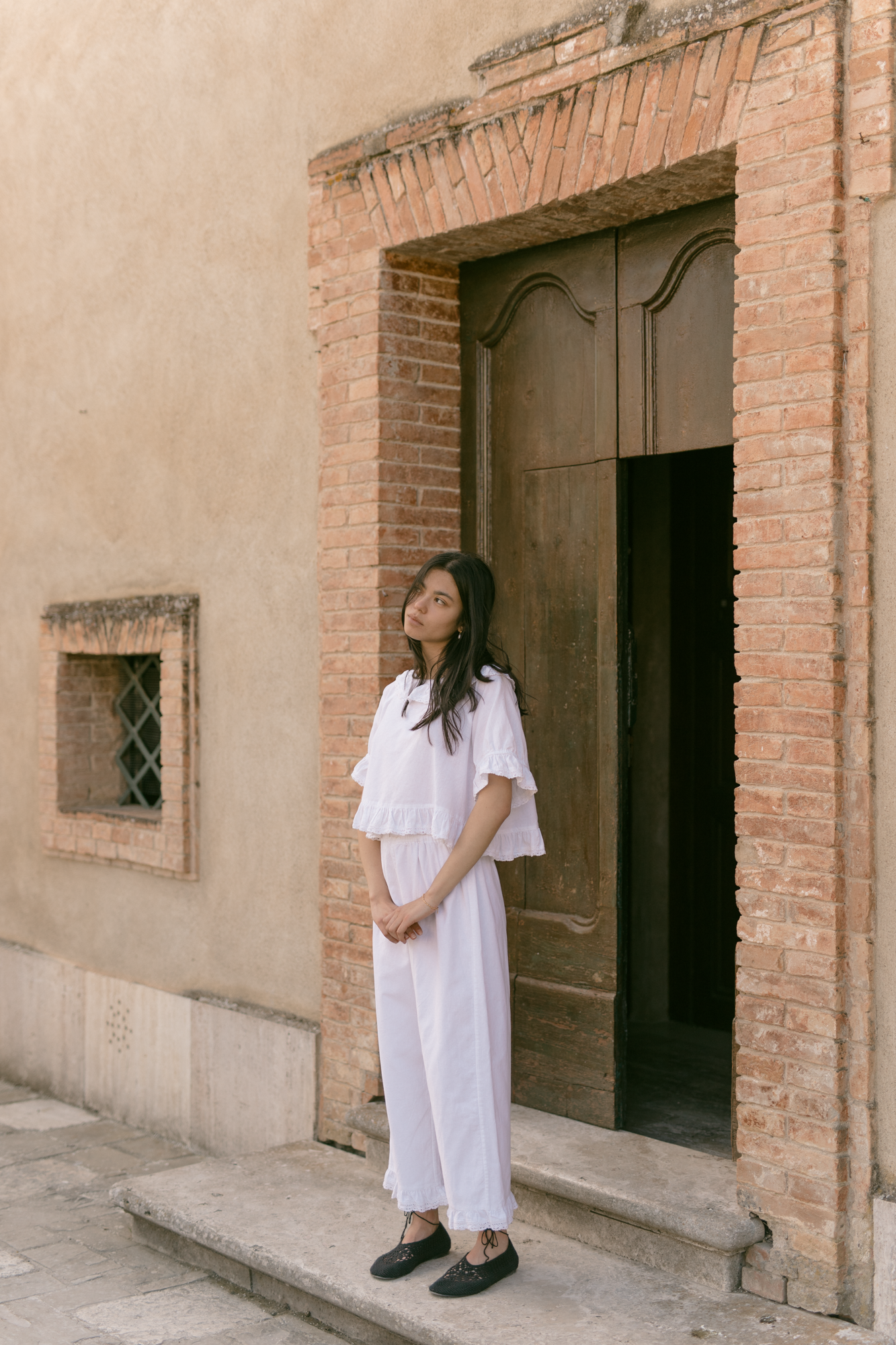 Model wearing the Arlette Pant in Salt by Gillian Stevens, full-length front view against a rustic brick doorway