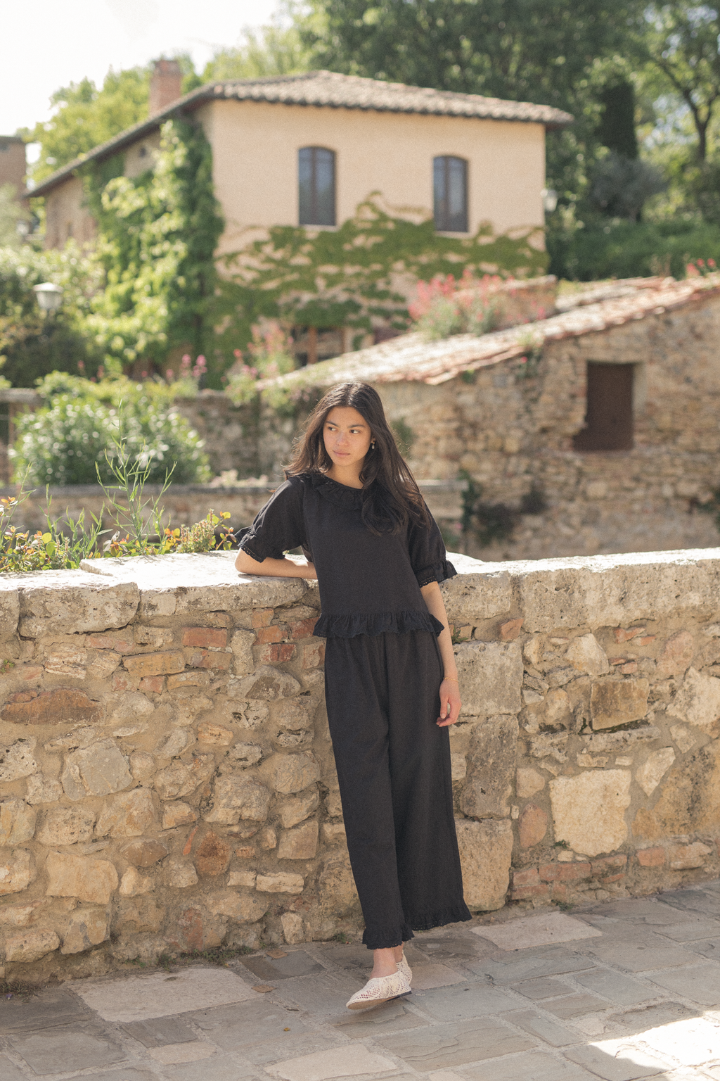 Model wearing the Arlette Pant in Noir by Gillian Stevens, full-length front view against a stone wall