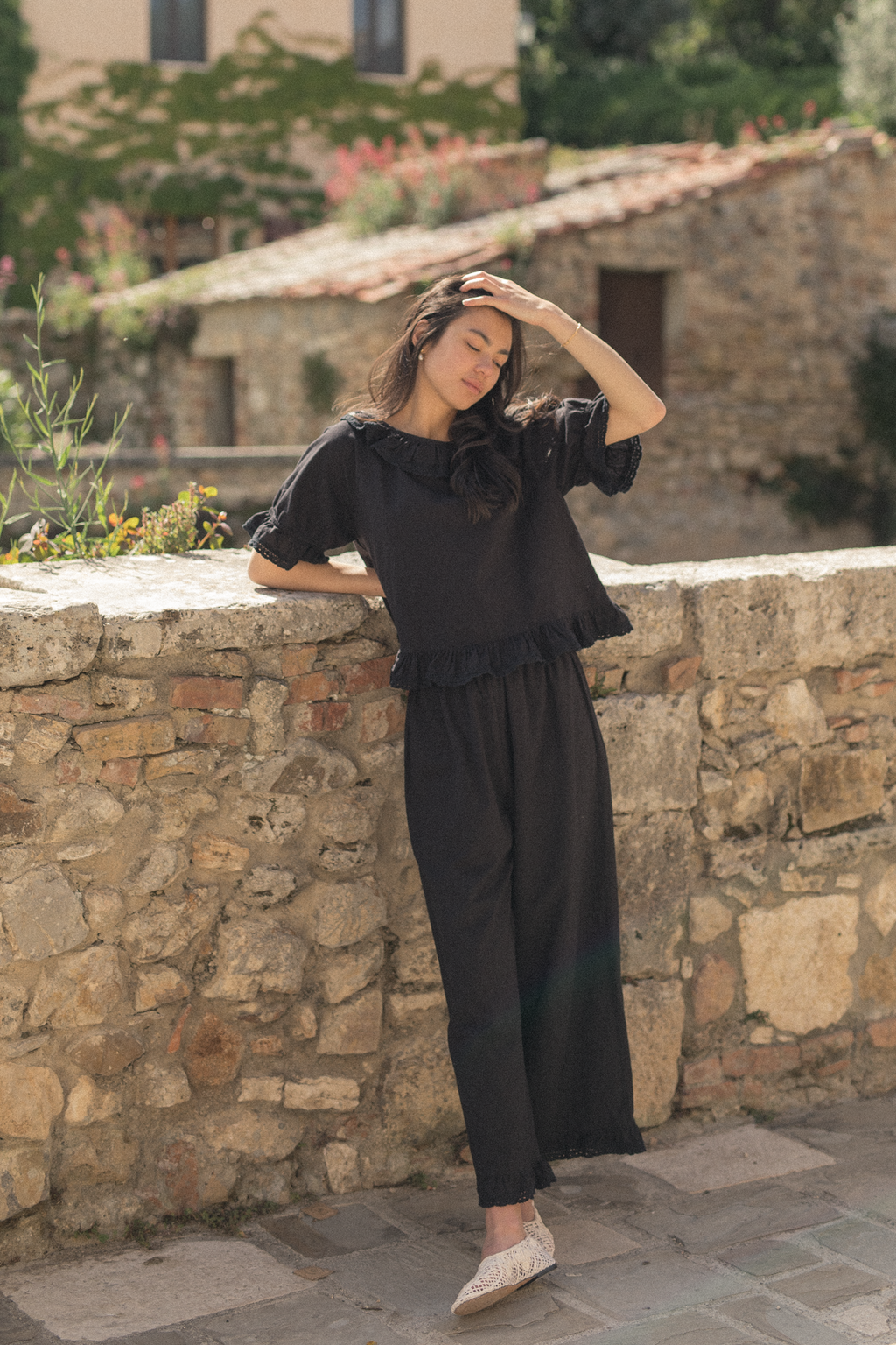 Model wearing the Arlette Pant in Noir by Gillian Stevens, full-length front view against a stone wall