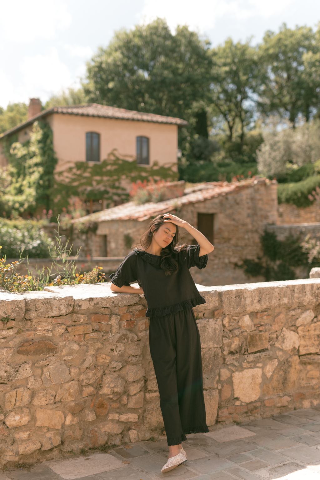 Model wearing the Arlette Pant in Noir by Gillian Stevens, full-length front view against a stone wall