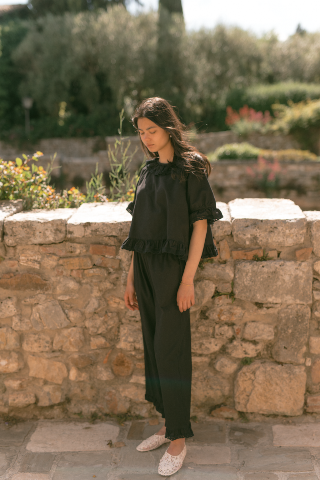 Model wearing the Arlette Pant in Noir by Gillian Stevens, full-length front view against a stone wall
