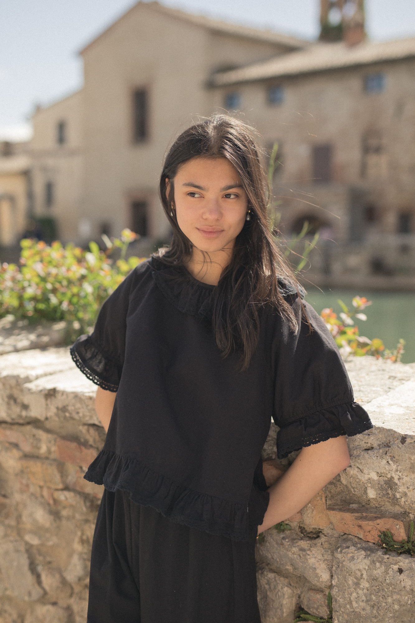 Model wearing the Arlette Top in Noir by Gillian Stevens, front view outdoors against a stone wall