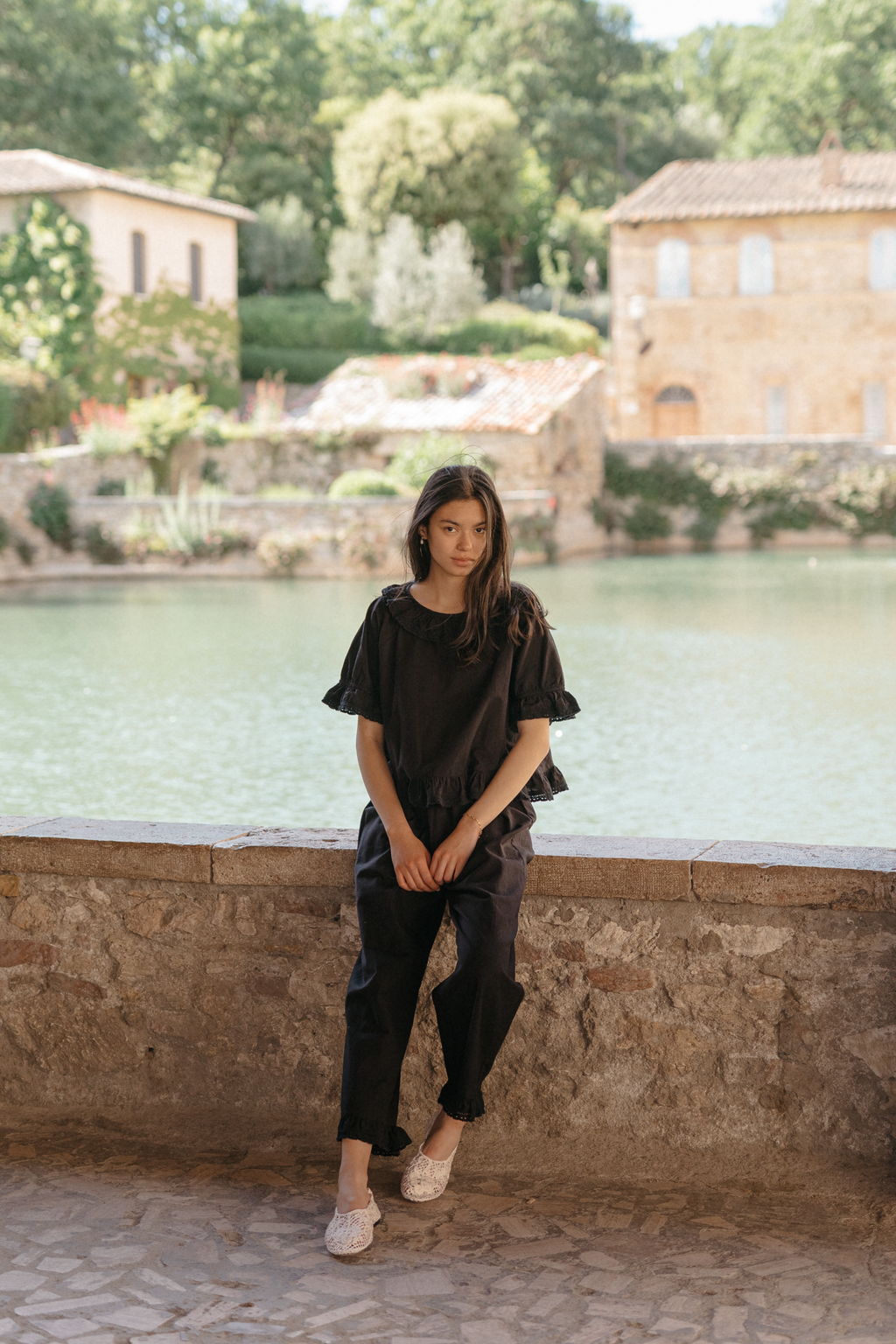 Model wearing the Arlette Pant in Noir by Gillian Stevens, styled with a matching top beside a Tuscan pool