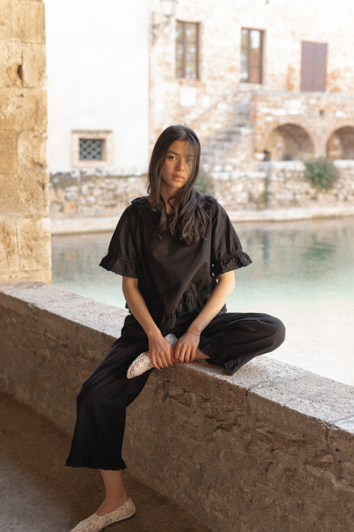 Model seated on stone ledge wearing the Arlette Top in Noir by Gillian Stevens, front view