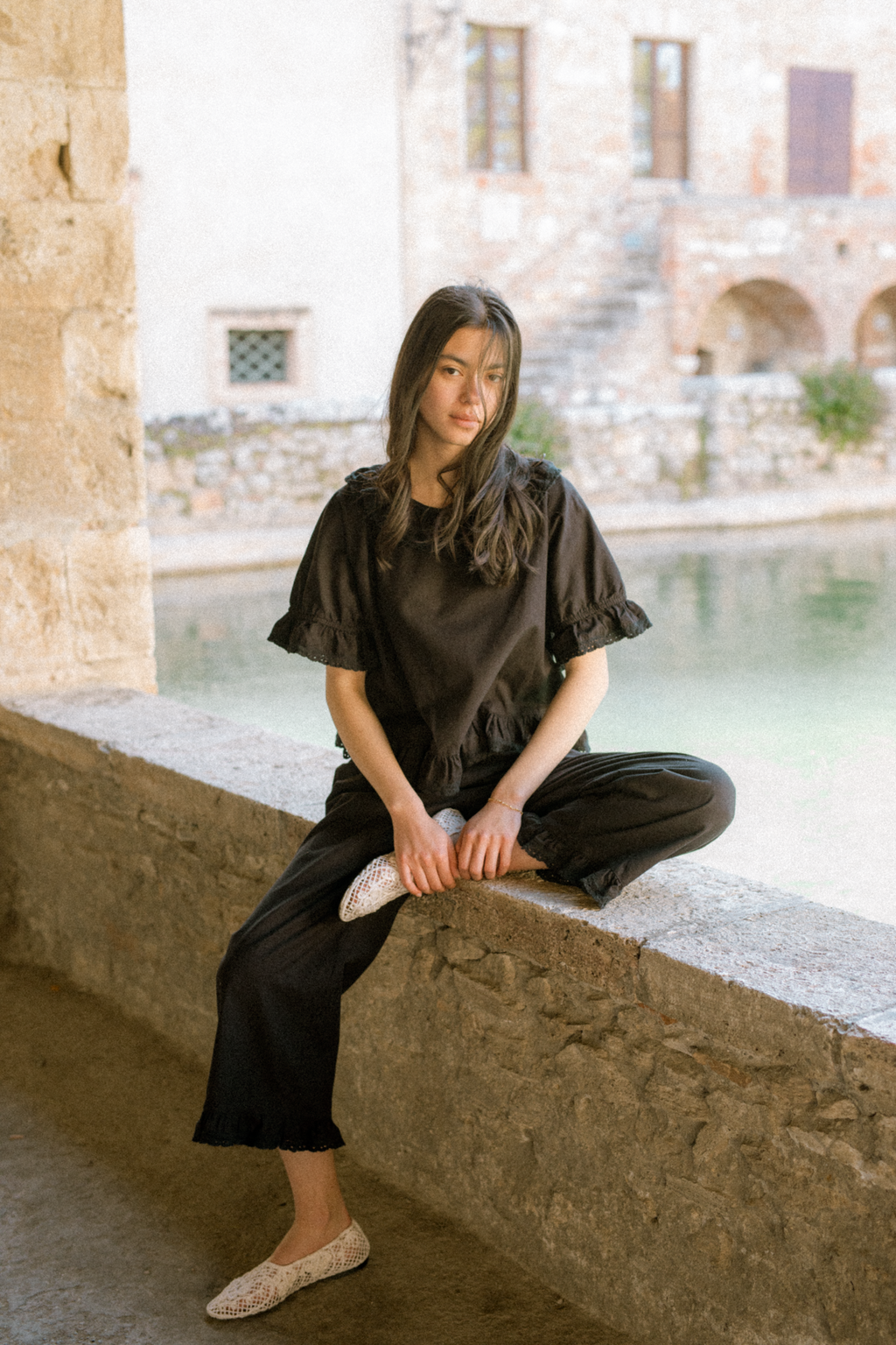 Model seated outdoors wearing the Arlette Top in Noir by Gillian Stevens, full-length view