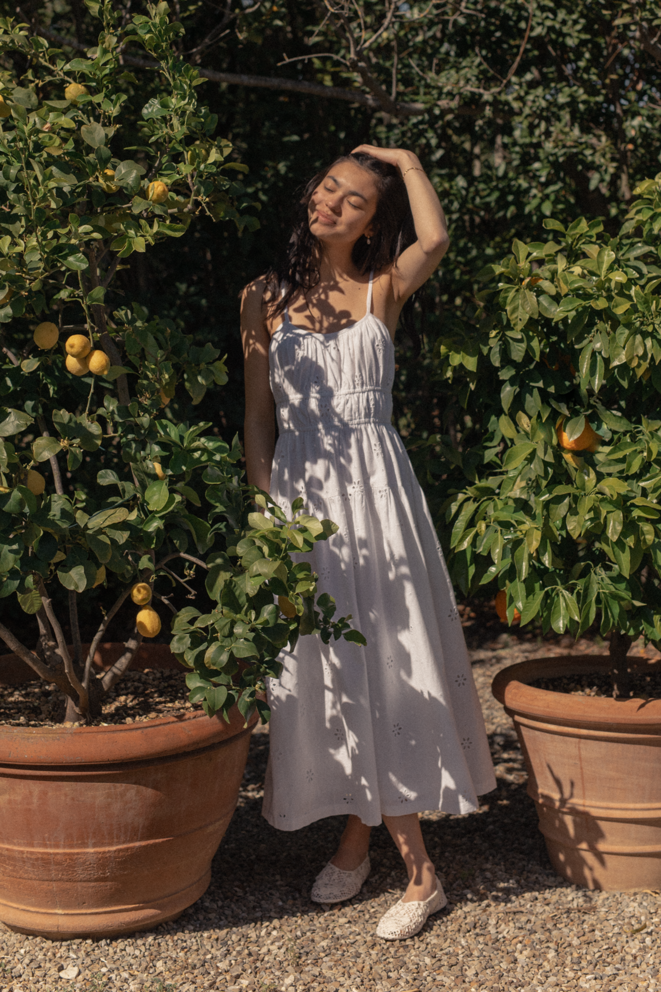 Model wearing the Alessandra Dress in Salt by Gillian Stevens, full-length front view among potted lemon trees