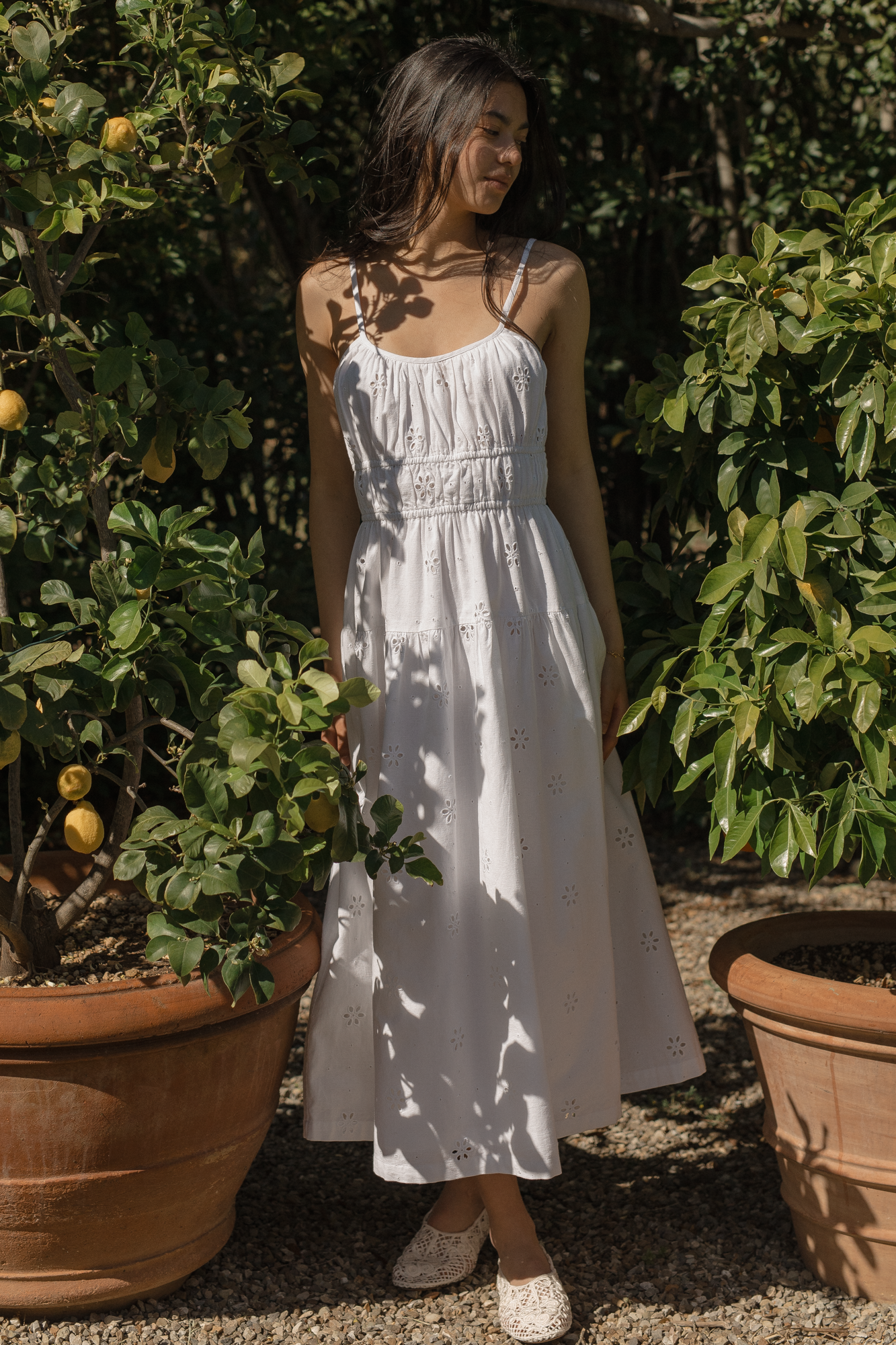Model wearing the Alessandra Dress in Salt by Gillian Stevens, front view among lemon trees in a sunlit garden