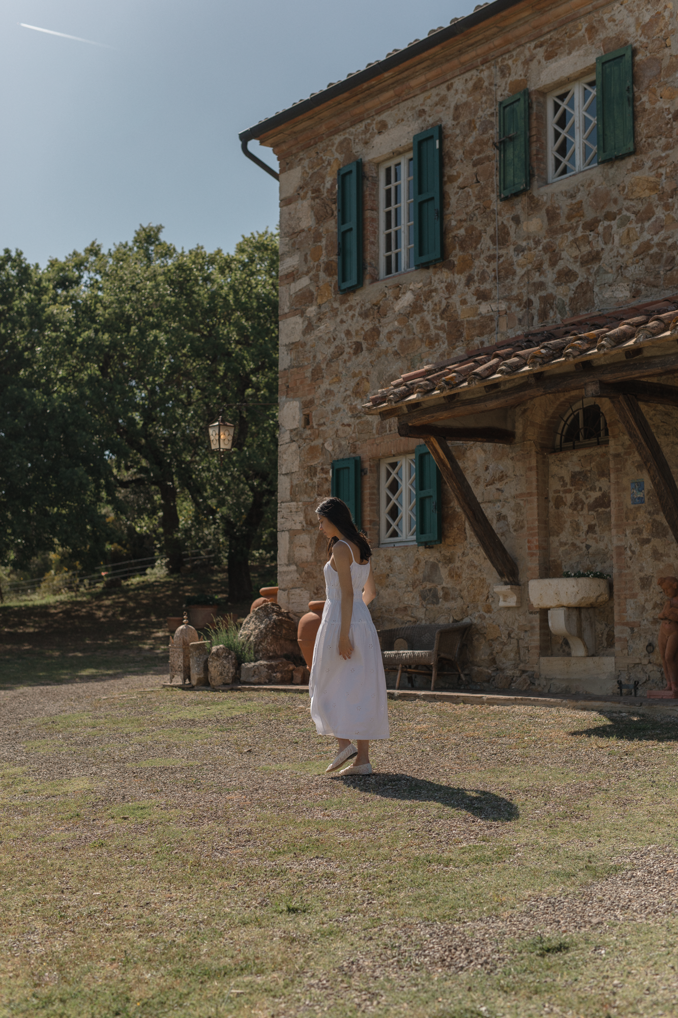 Model wearing the Alessandra Dress in Salt by Gillian Stevens, side view outside a rustic stone villa