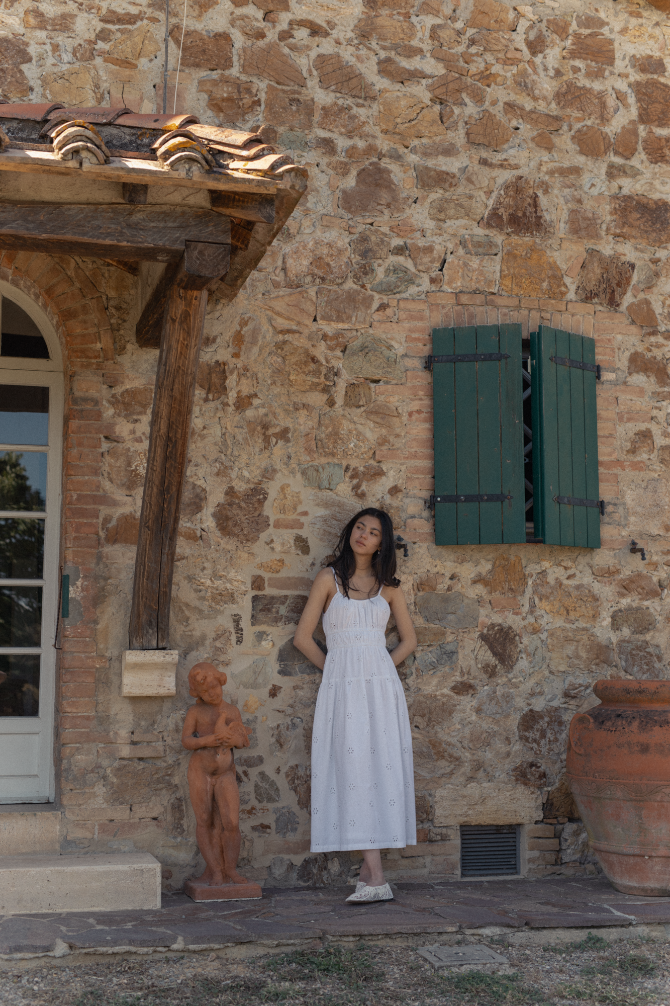Model wearing the Alessandra Dress in Salt by Gillian Stevens, full-length front view against a rustic stone wall