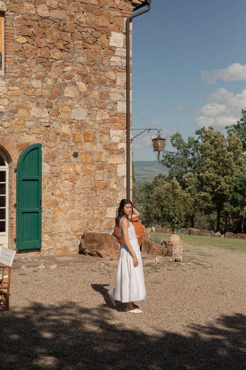 Model wearing the Plum Dress in Salt by Gillian Stevens, full-length view outside a Tuscan stone villa