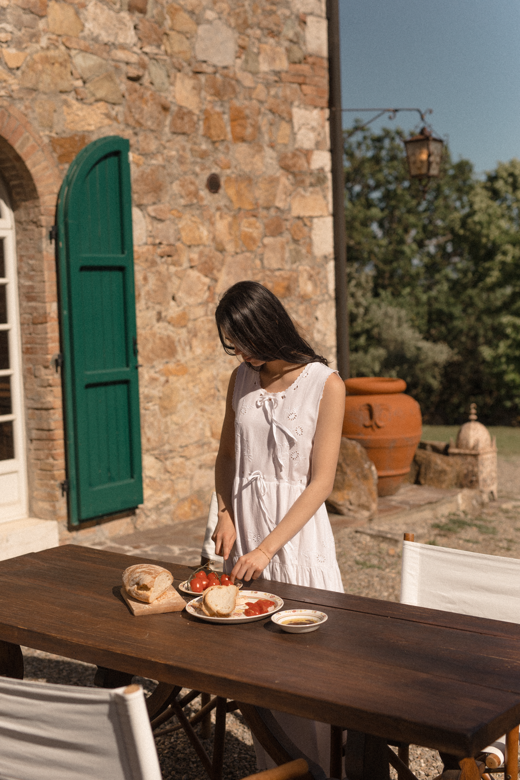 Model wearing the Plum Dress in Salt by Gillian Stevens, front view at an outdoor Tuscan table