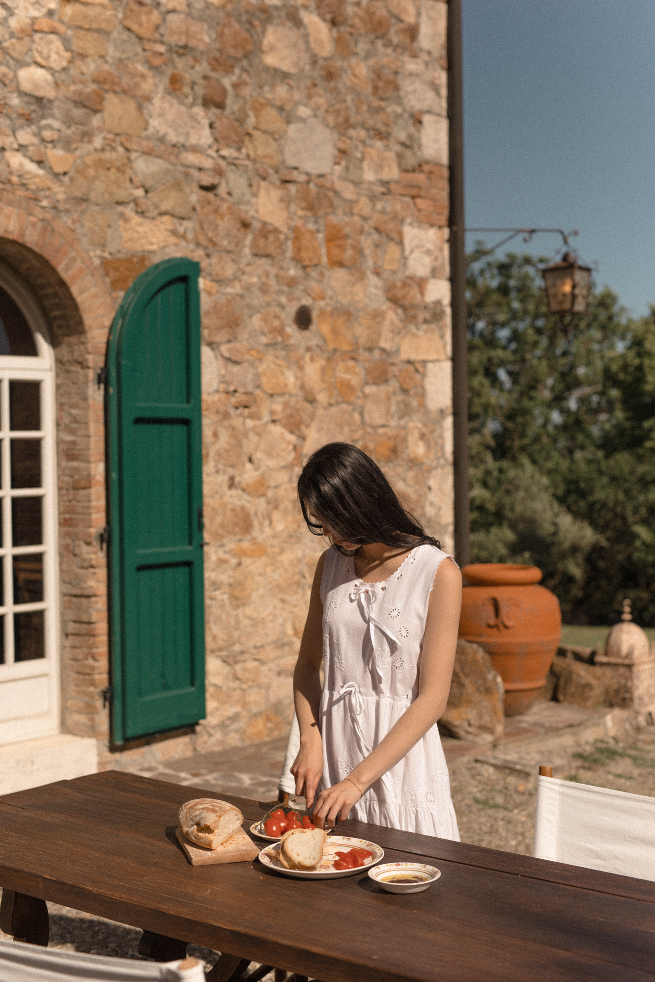Model wearing the Plum Dress in Salt by Gillian Stevens, outdoors at a rustic Tuscan stone villa