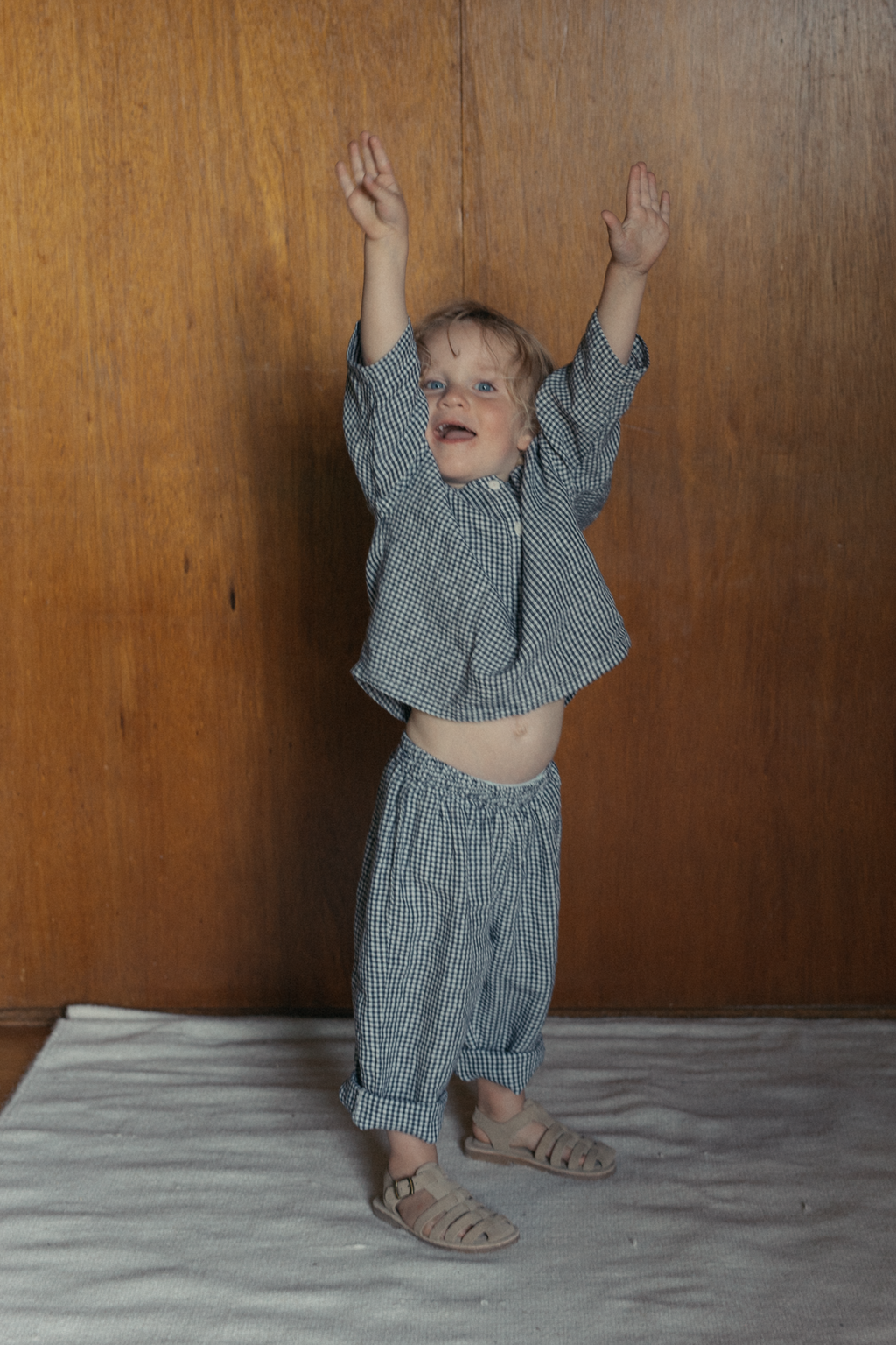 Child wearing the Bertie Pant in Marine Gingham by Gillian Stevens, full-length front view with arms raised