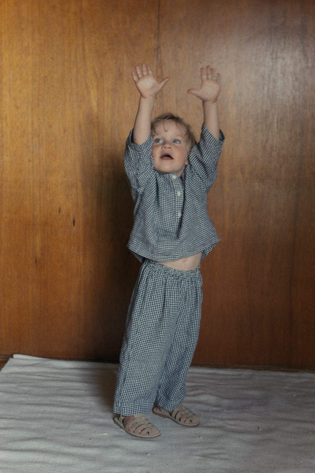 Child wearing the Bertie Pant in Marine Gingham by Gillian Stevens, full-length front view with arms raised