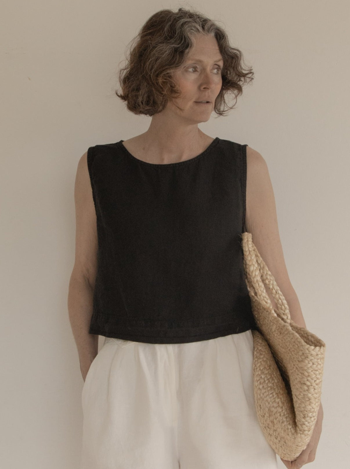 Model wearing the Finley Top in Noir by Gillian Stevens, front view styled with white trousers and a woven bag
