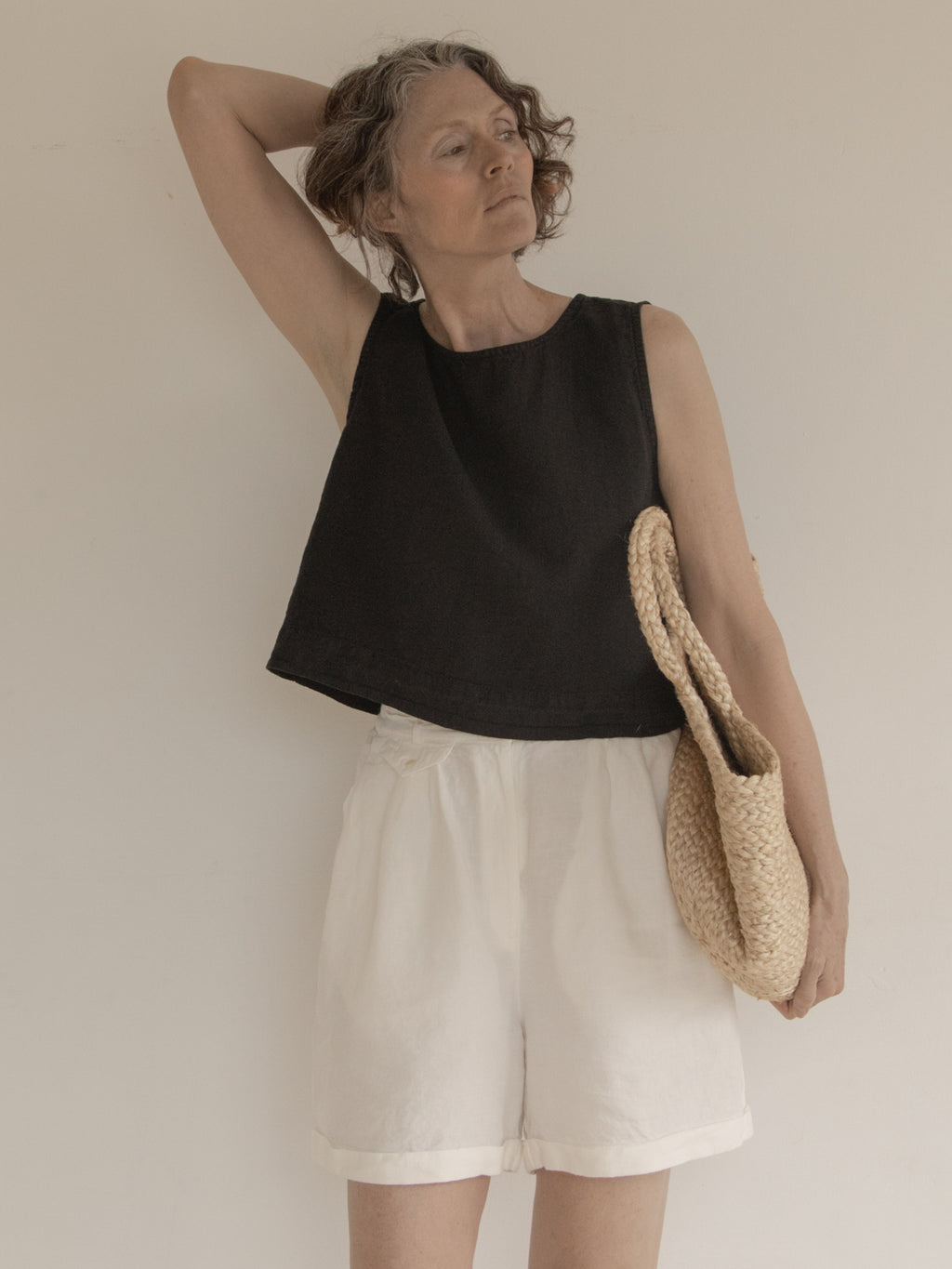 Model wearing the Finley Top in Noir by Gillian Stevens, front view styled with white shorts and woven bag