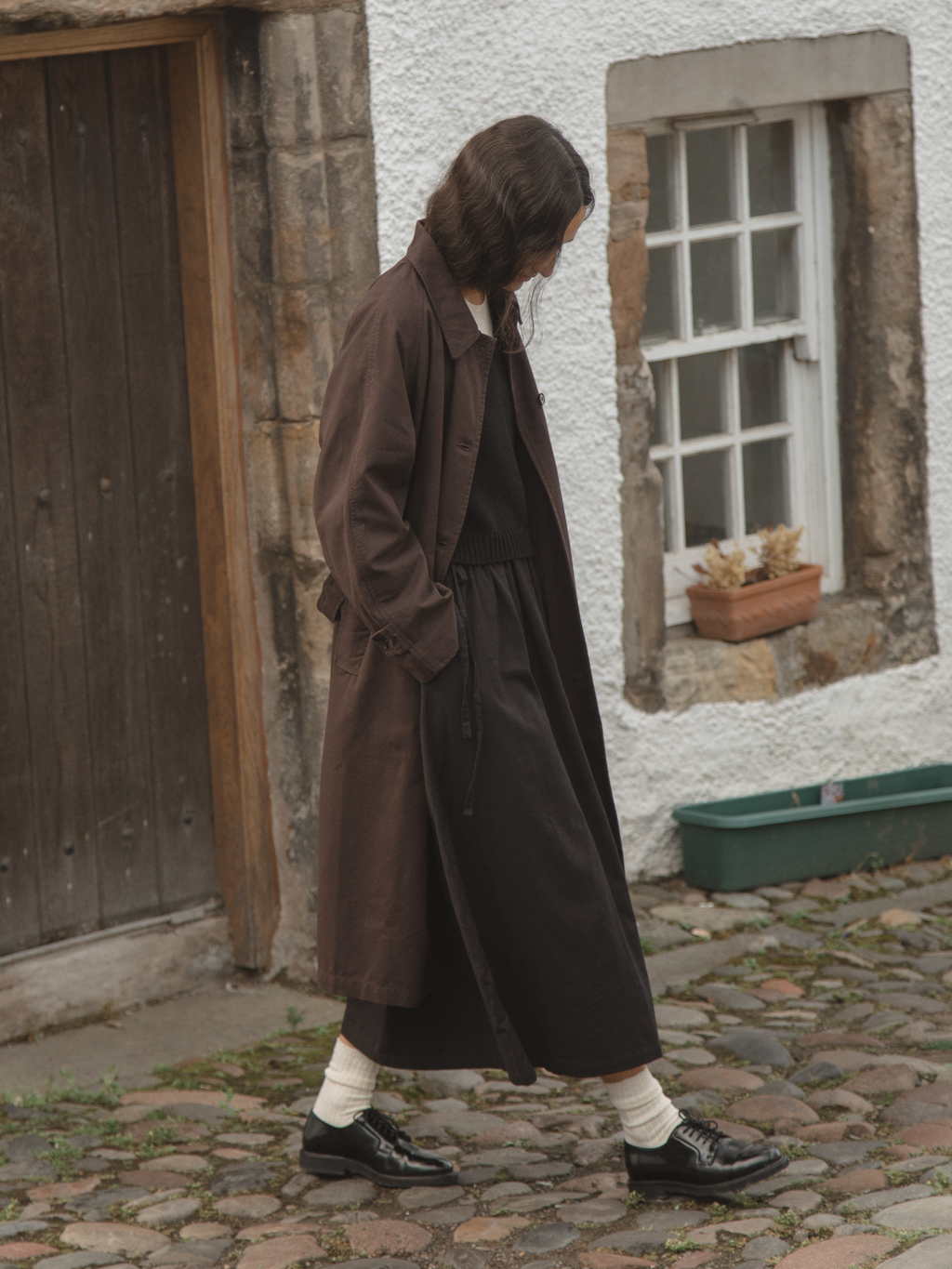 Model wearing the Penelope Trench in Espresso by Gillian Stevens, side view on cobblestone street