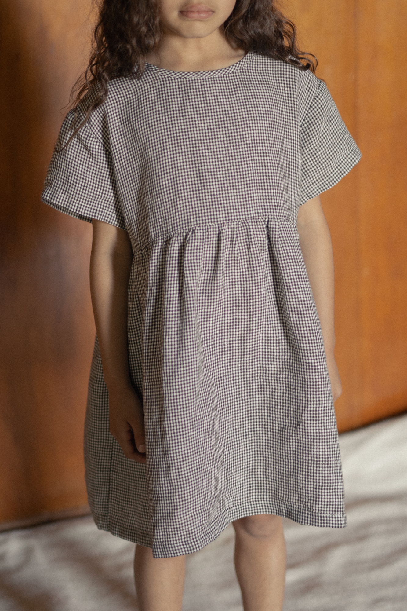 Child wearing the Mini Aya in Espresso Gingham by Gillian Stevens, front view showing gathered waist and short sleeves