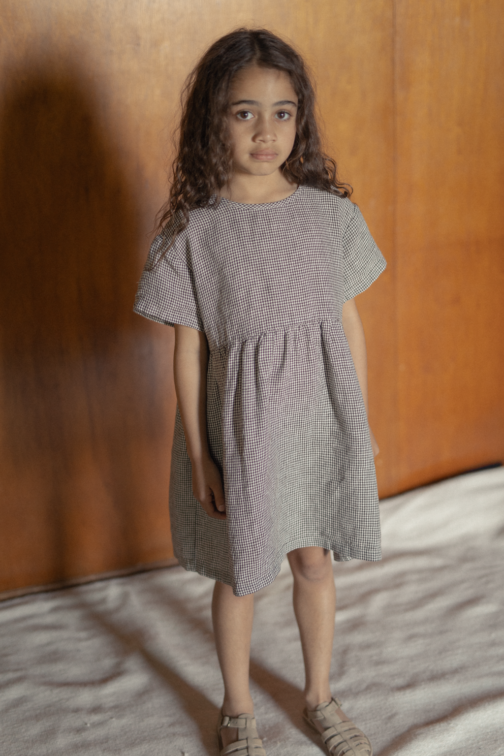 Child wearing the Mini Aya in Espresso Gingham by Gillian Stevens, front view showing gathered waist and short sleeves