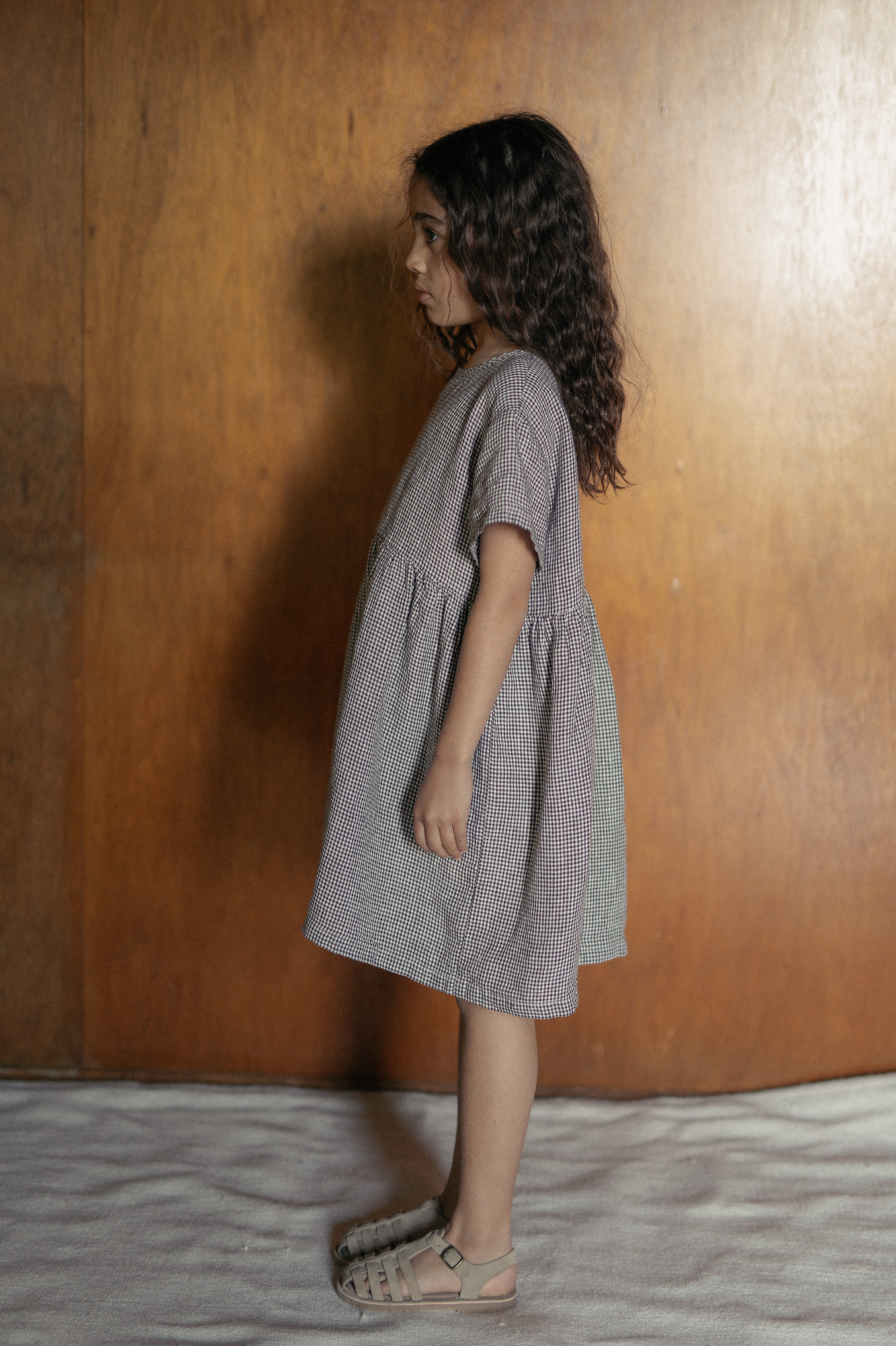 Child wearing the Mini Aya in Espresso Gingham by Gillian Stevens, side view showing gathered skirt and short sleeves