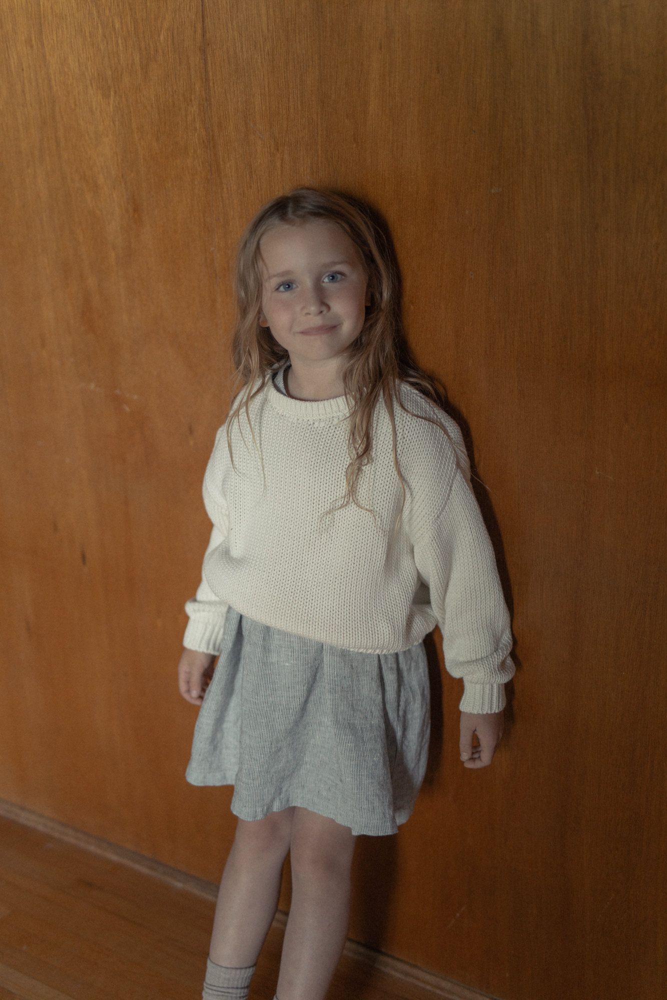 Child wearing the Mini Townes Pullover in Alabaster by Gillian Stevens, front view against a warm timber wall