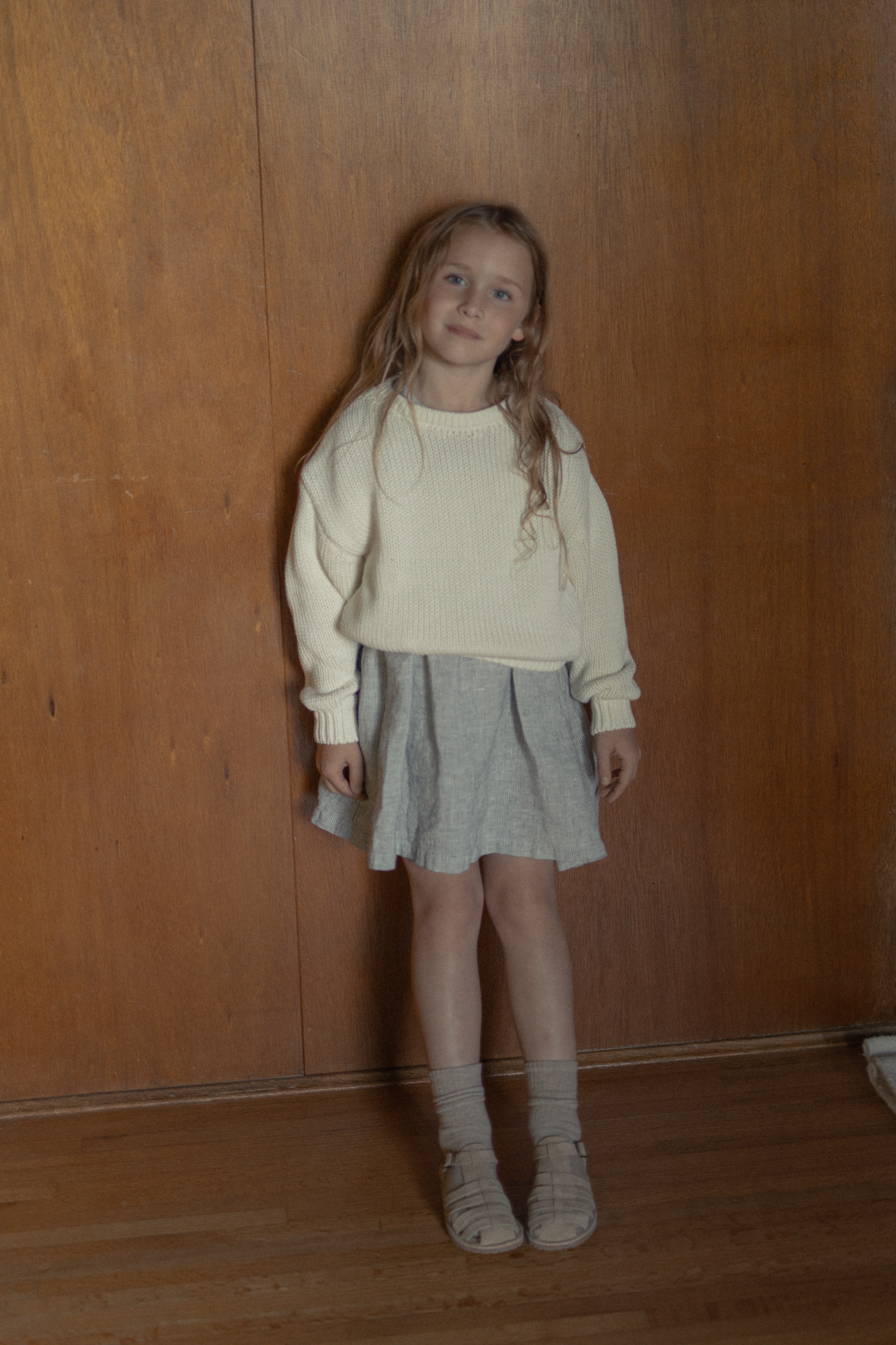 Child wearing the Mini Townes Pullover in Alabaster by Gillian Stevens, front view styled with a skirt